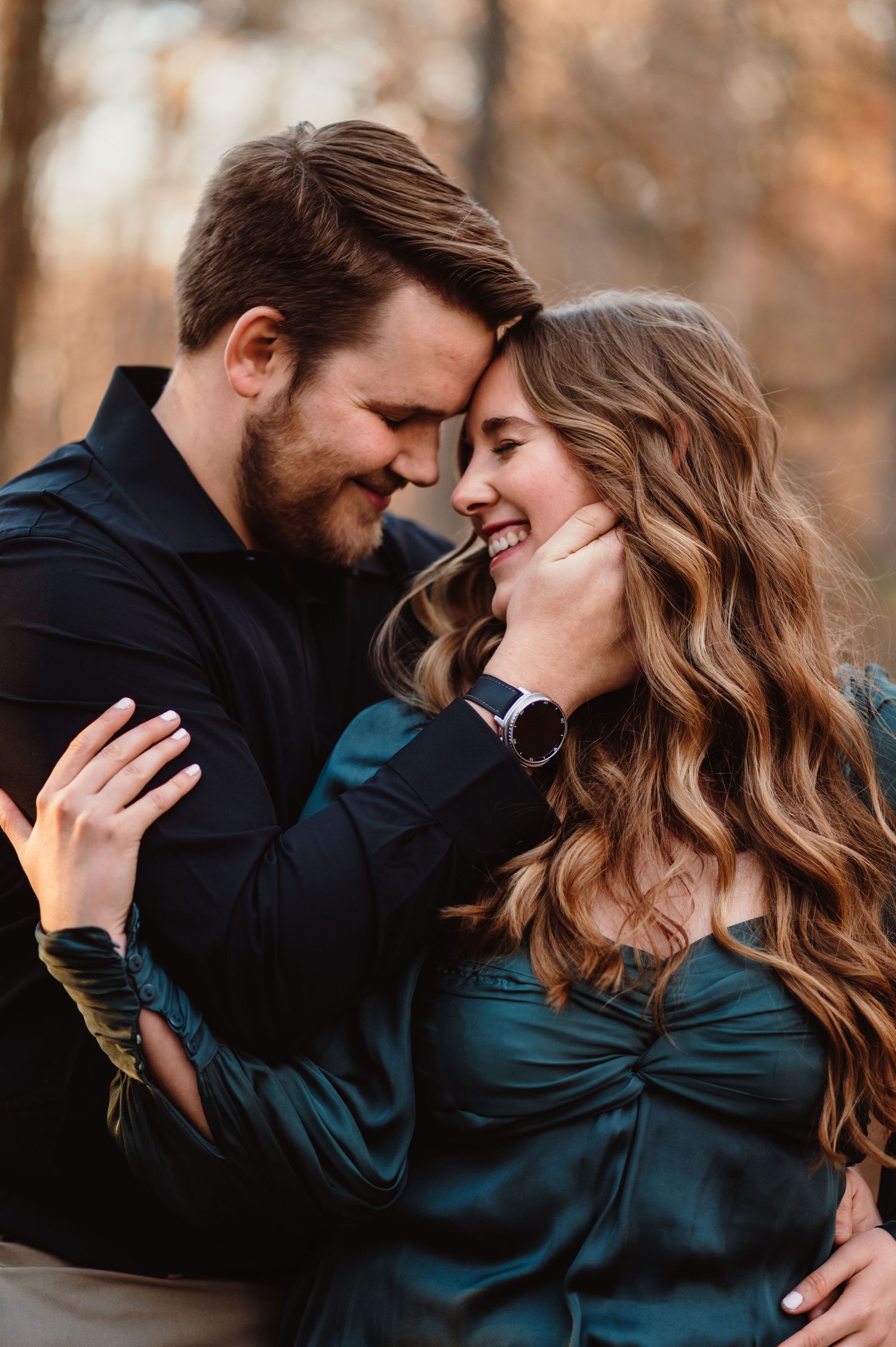 Happy couple embraces forehead to forehead, smiling together in an autumn outdoor setting.