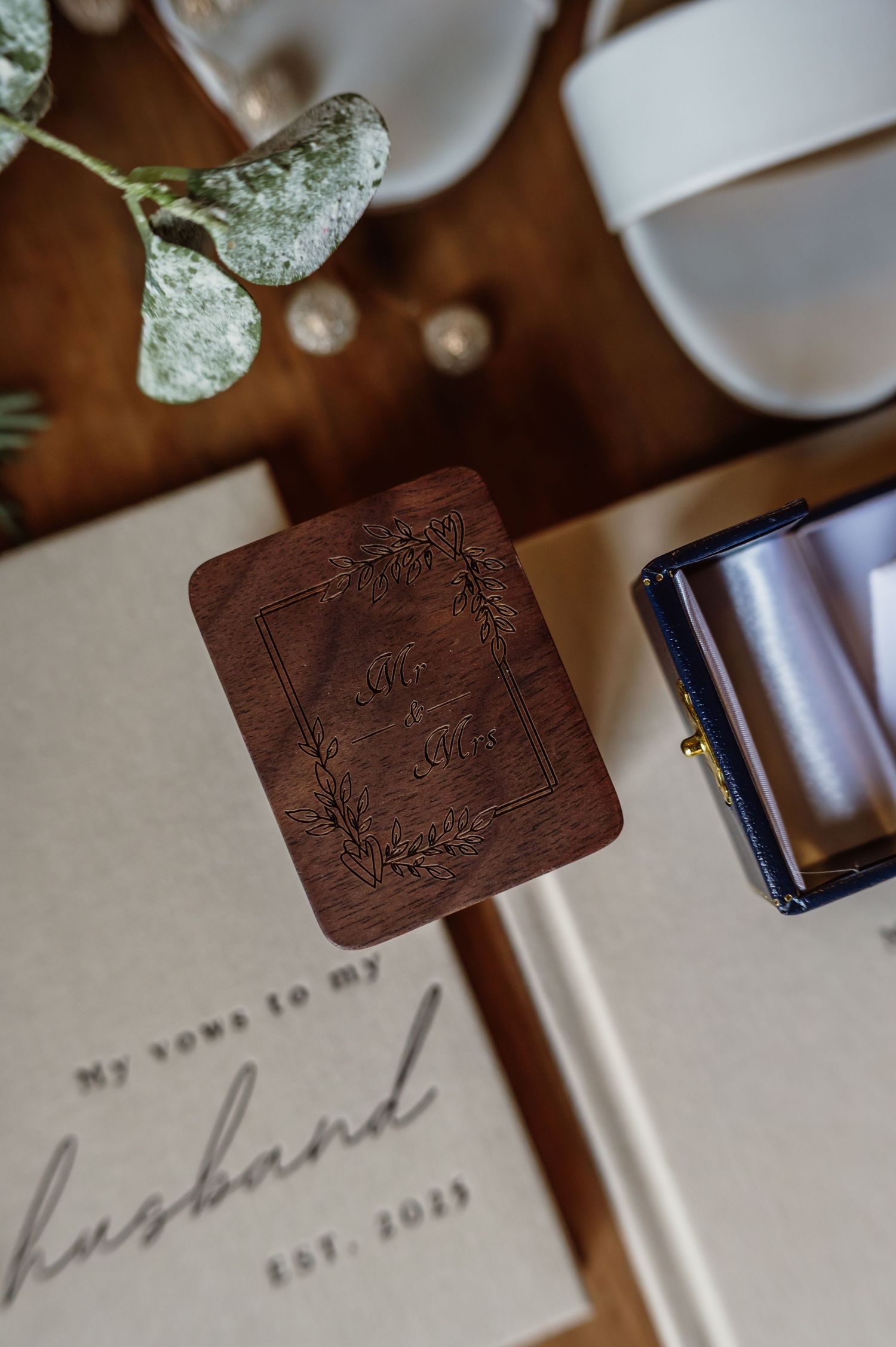 Wooden engraved vow card with floral frame beside a vow book reading 'my vows to my husband est. 2023' and ring box.
