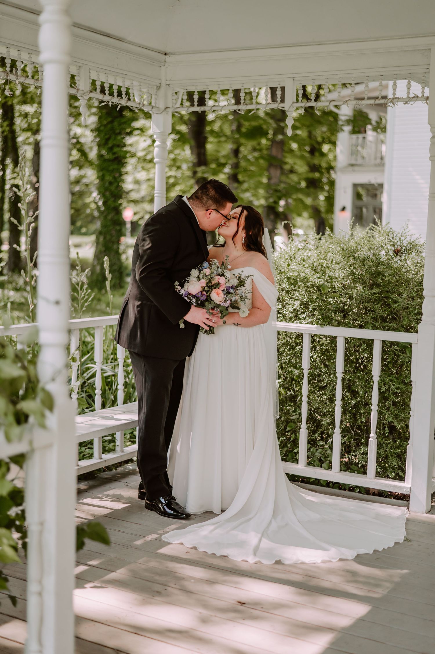 Bride and groom share a kiss on a white gazebo porch at The Red Barn at Sycamore Farm. Terre Haute Wedding Photographer