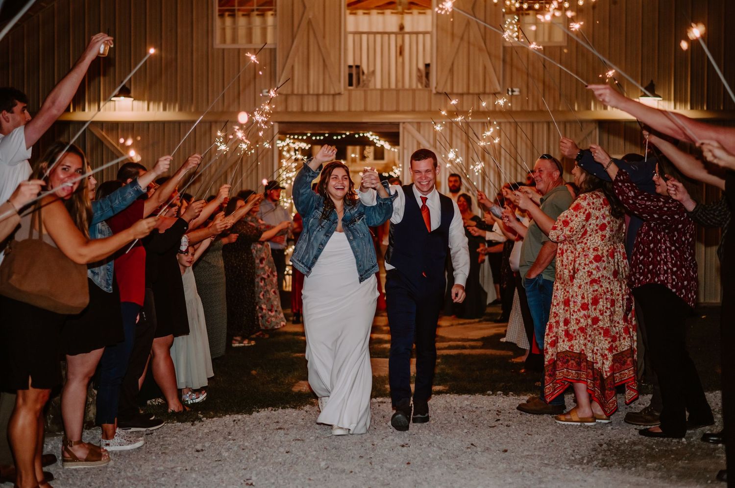 Bride and groom walk through sparkler exit tunnel at Laurel Mill Wedding Barn with guests celebrating. Indianapolis wedding photographer