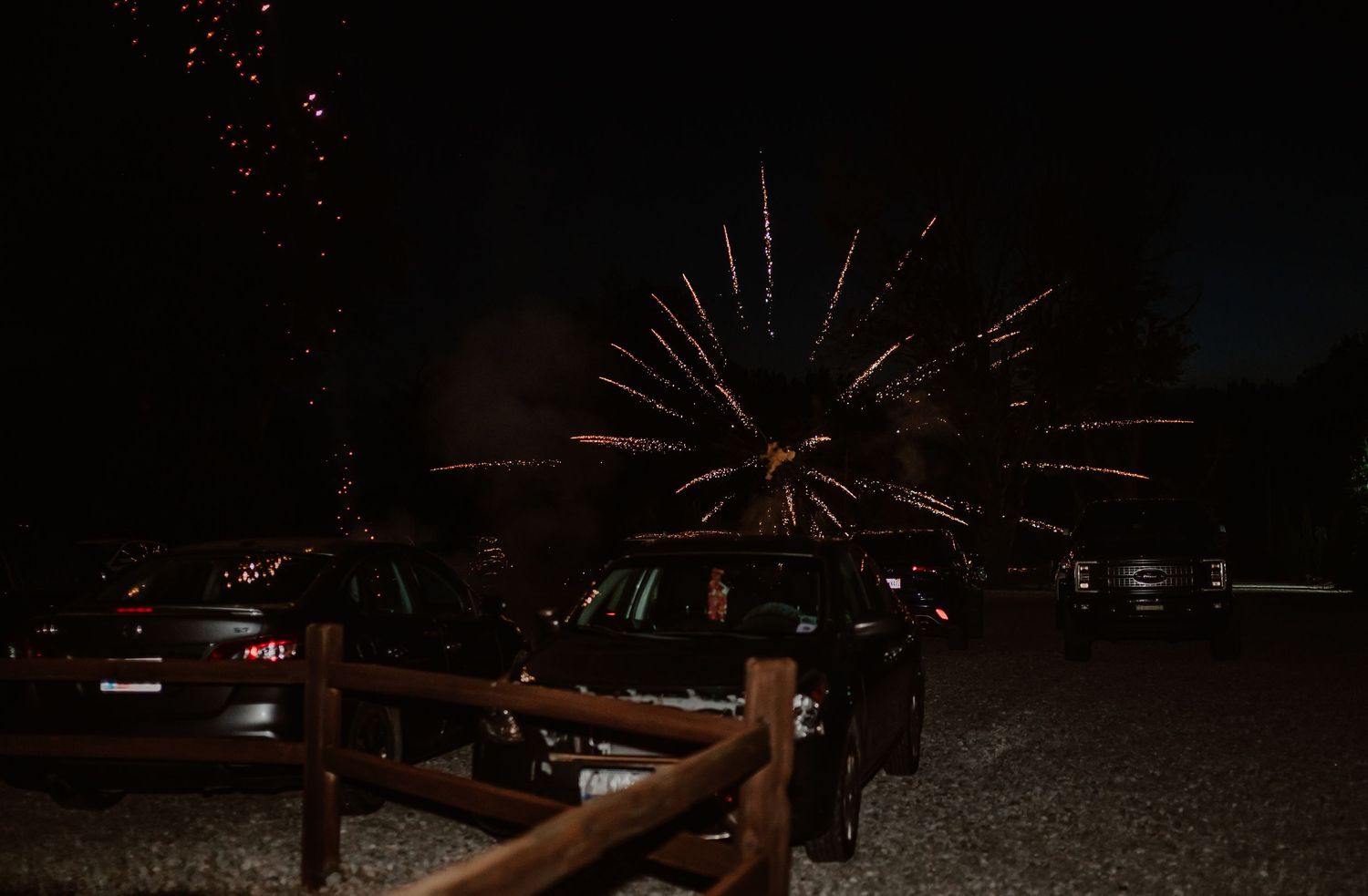 Colorful fireworks burst in night sky above parked cars at outdoor wedding venue celebration.
