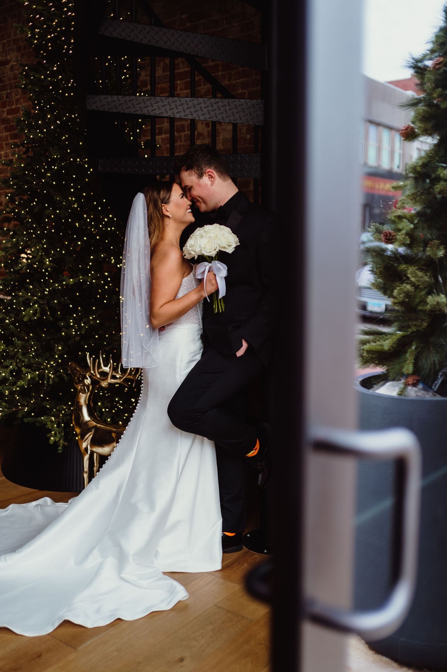 Bride and groom share a romantic moment near a Christmas tree, bride holding white bouquet in elegant mermaid gown.
