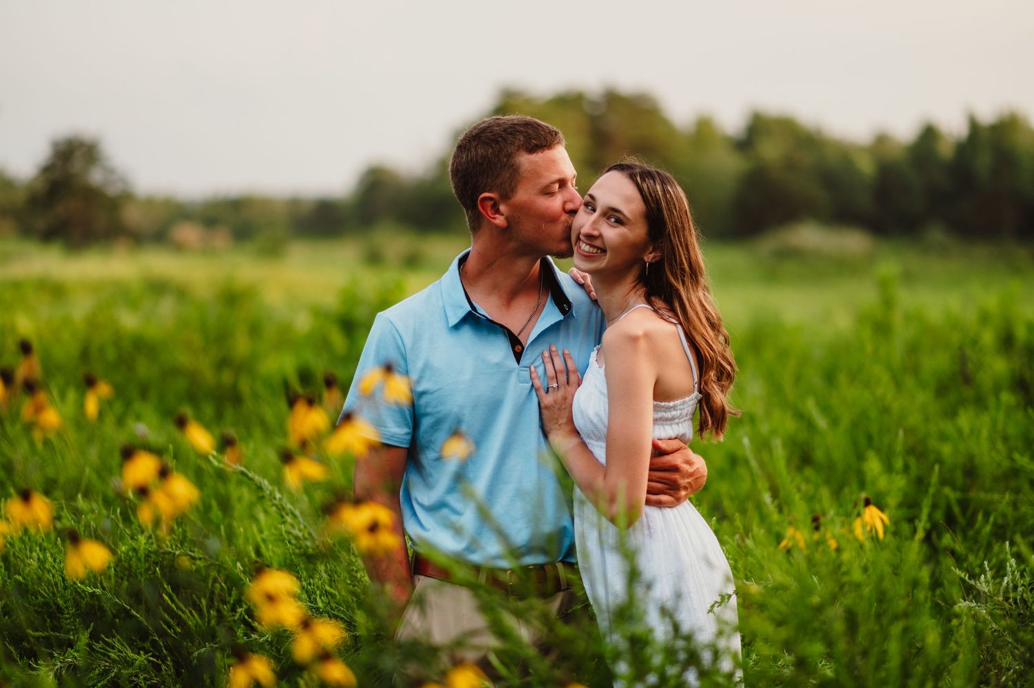 Happy couple posing in a lush green meadow with yellow wildflowers, sharing a tender kiss.
