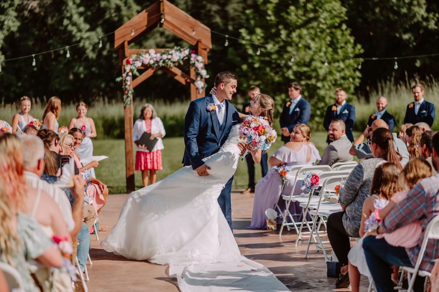 Groom twirls bride in white gown during joyful outdoor wedding ceremony recessional.