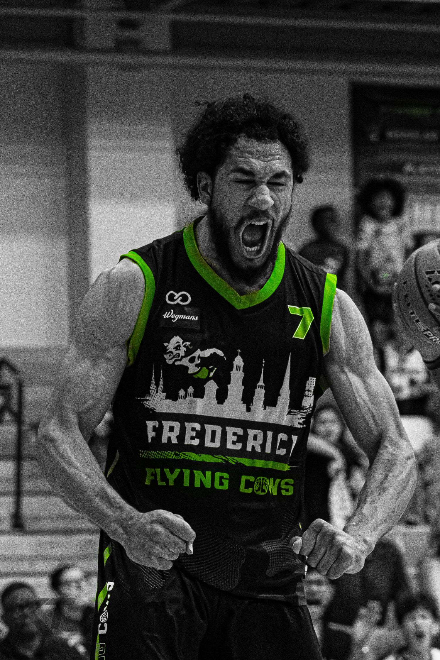 A Frederick Flying Cows basketball player celebrates intensely, wearing a black and green jersey with number 7.