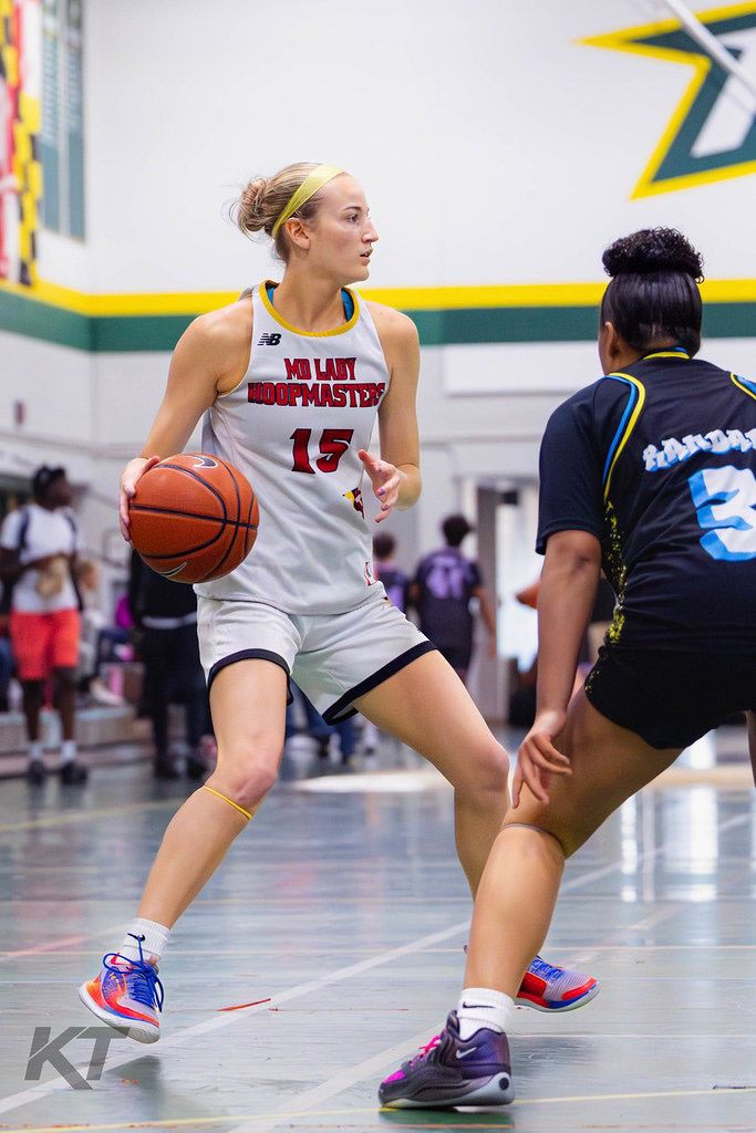 Female basketball player number 15 in MD Lady Hoopmasters white uniform dribbles past defender during indoor game.