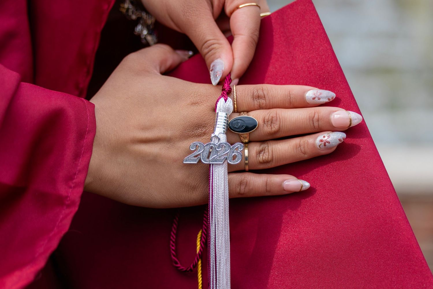 Close-up of graduate hands holding red mortarboard with 2023 charm tassel and decorated acrylic nails.