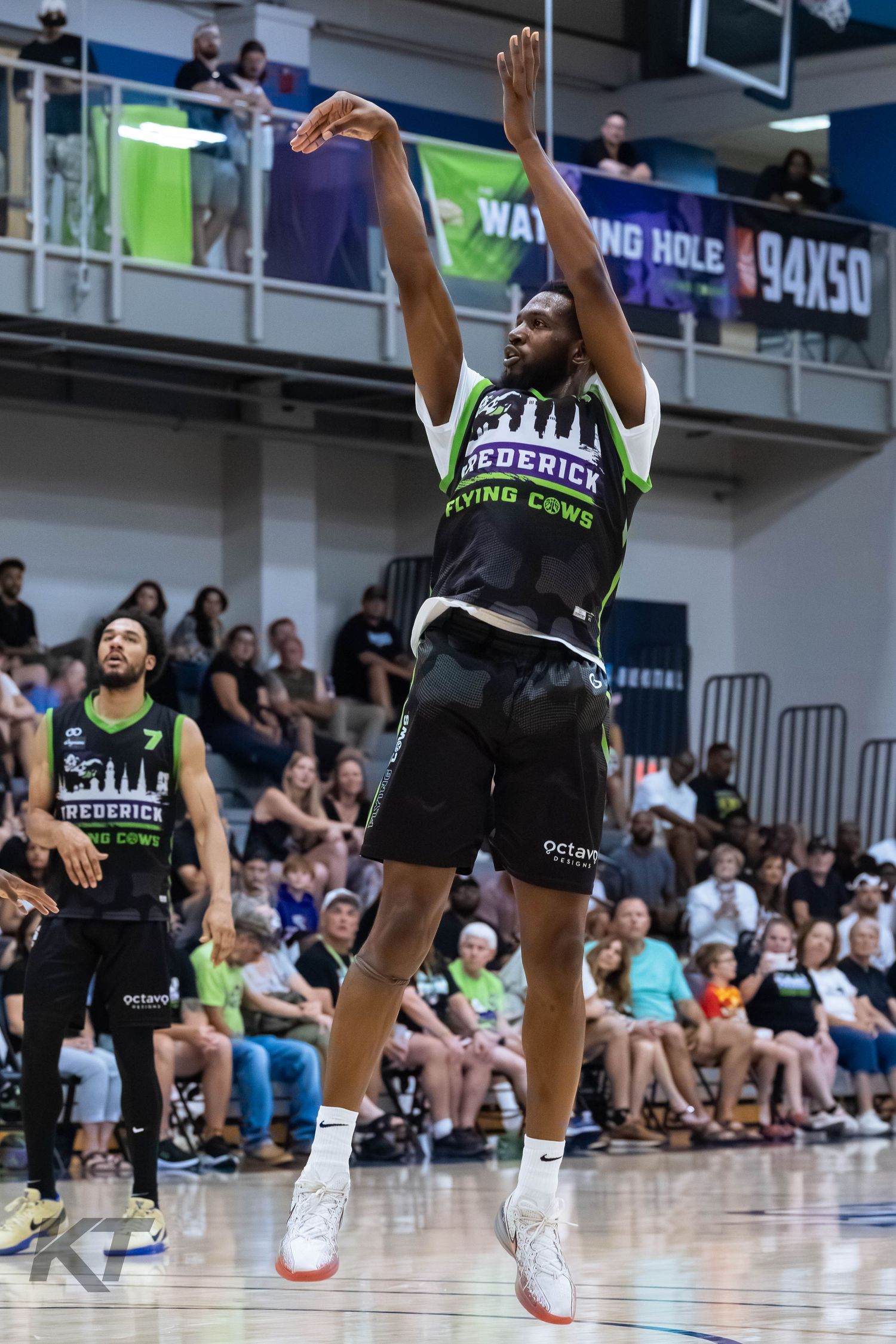 Frederick Flying Cows basketball player jumps to shoot during a packed arena game wearing black and green uniform.