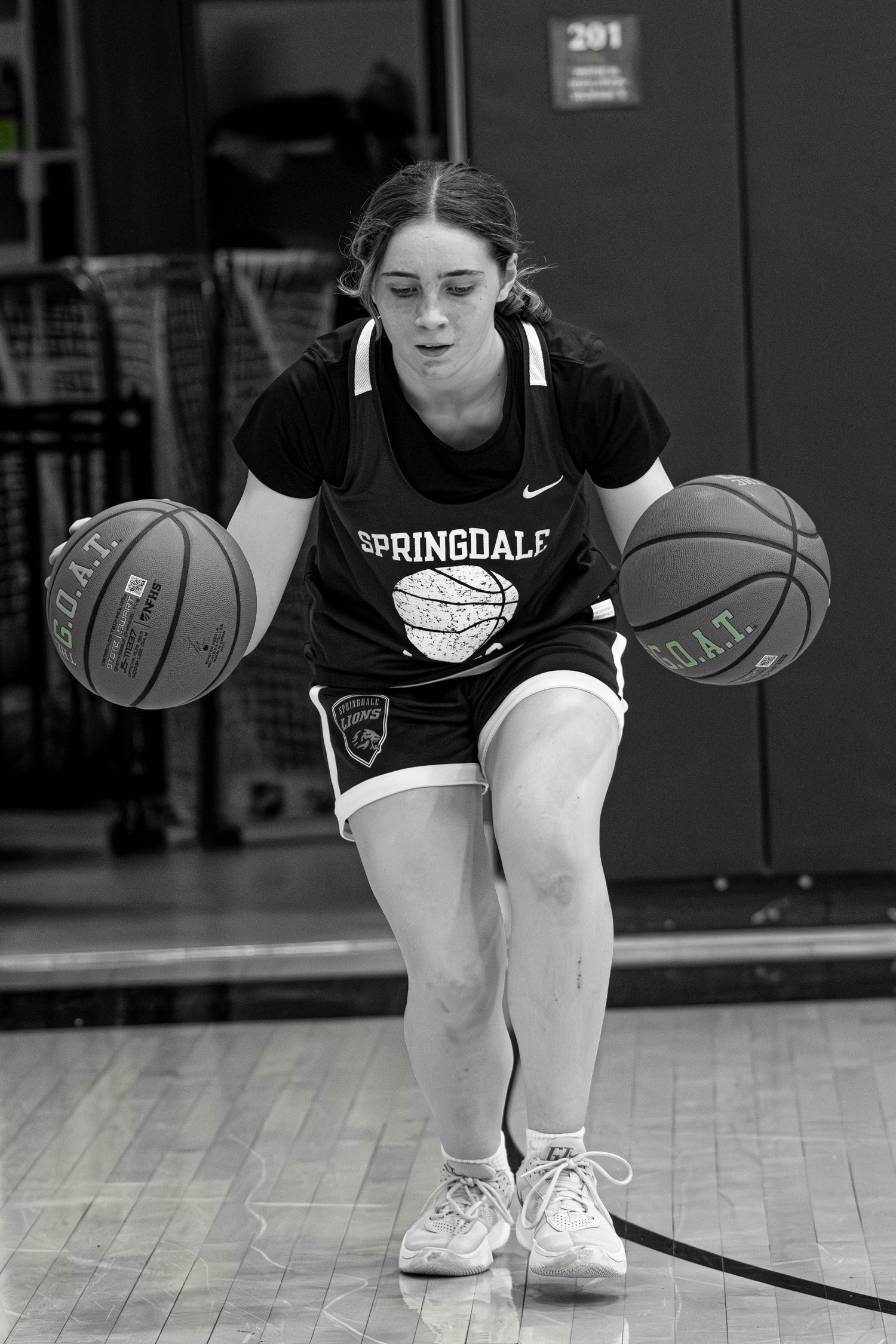 Girl in Springdale jersey dribbling two basketballs simultaneously during practice drill in black and white photo.