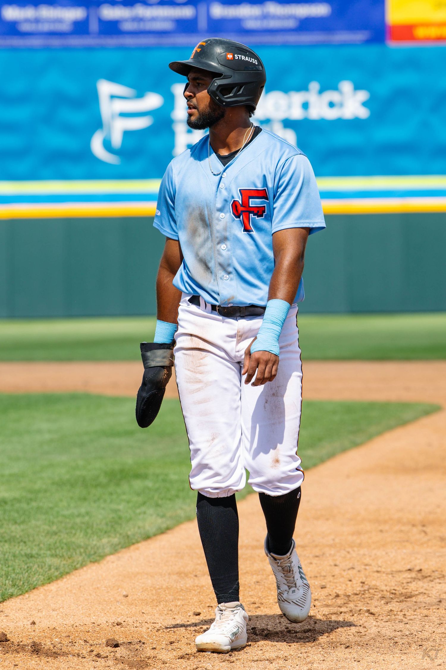 Baseball player in light blue Frederick jersey stands on base during a sunny minor league game.