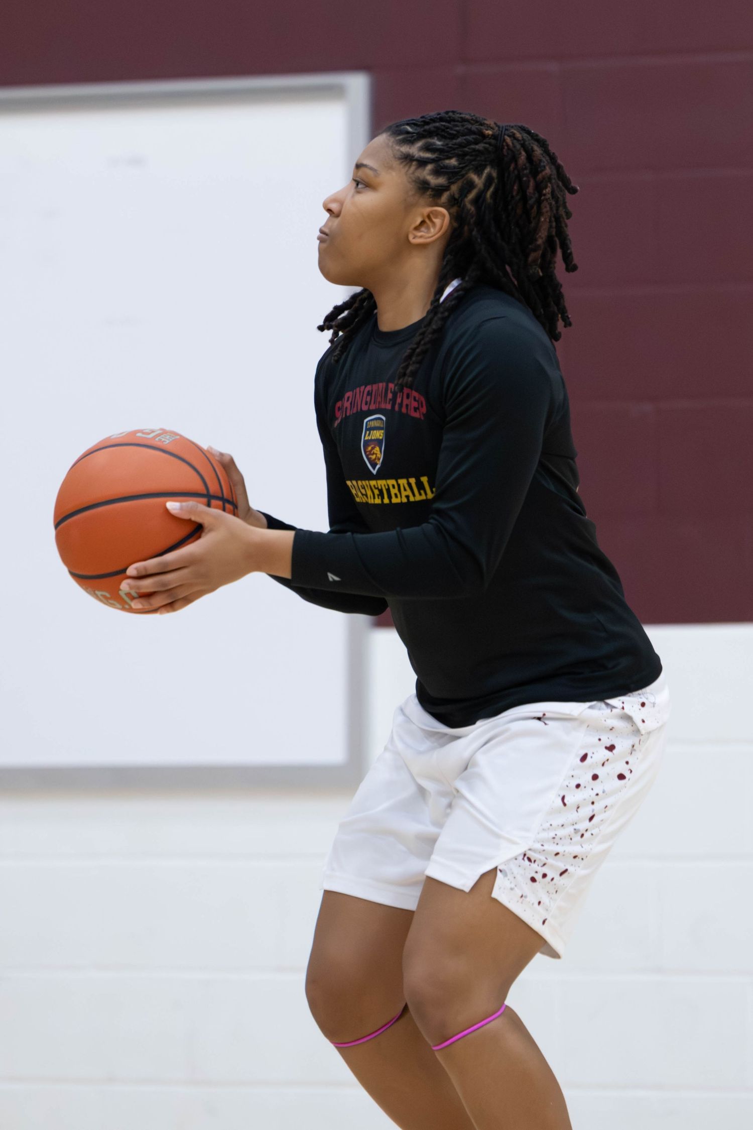 Young female basketball player in black jersey holds ball, preparing to shoot on indoor court.