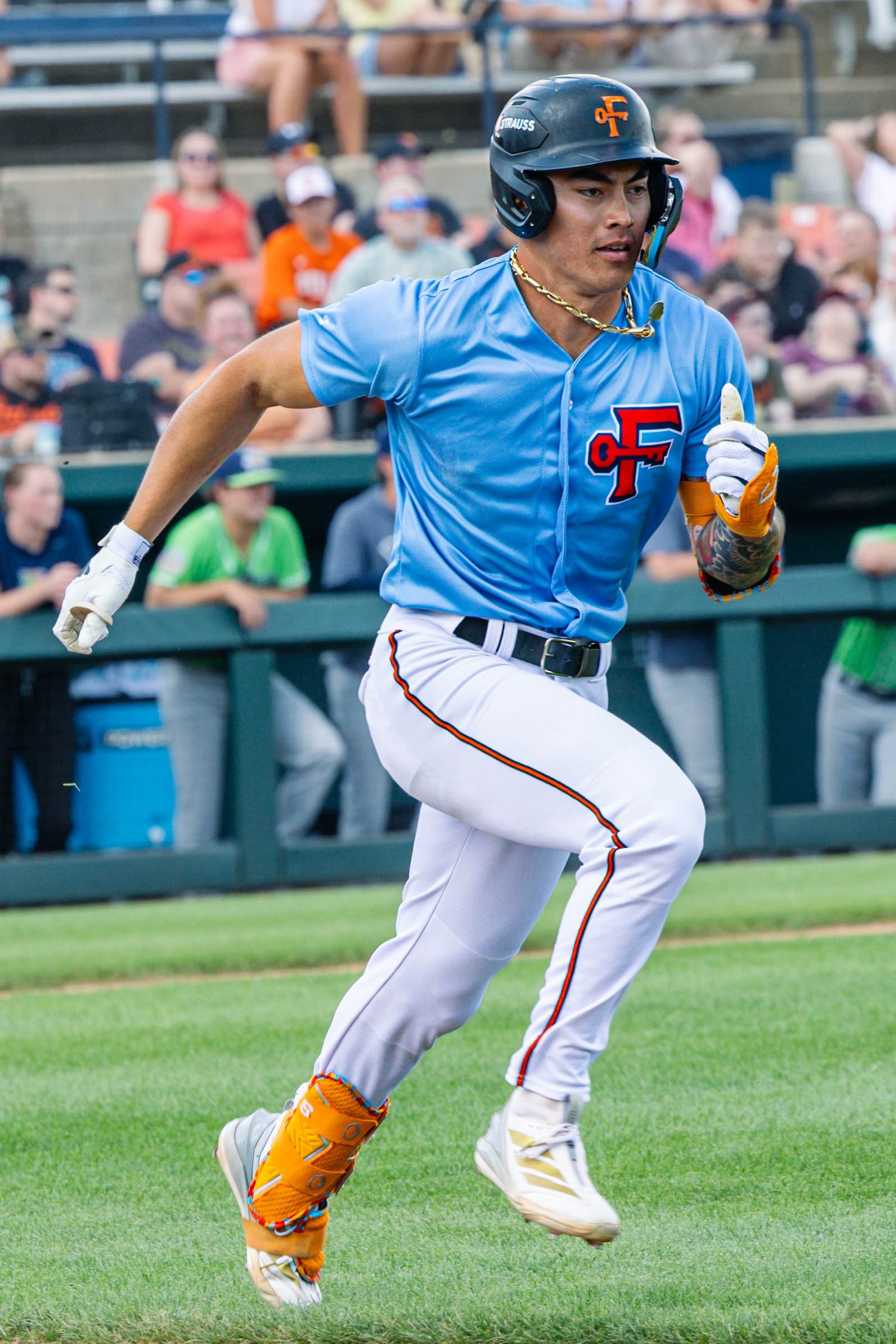 Baseball player in light blue CF jersey and white pants runs the bases during a minor league game.