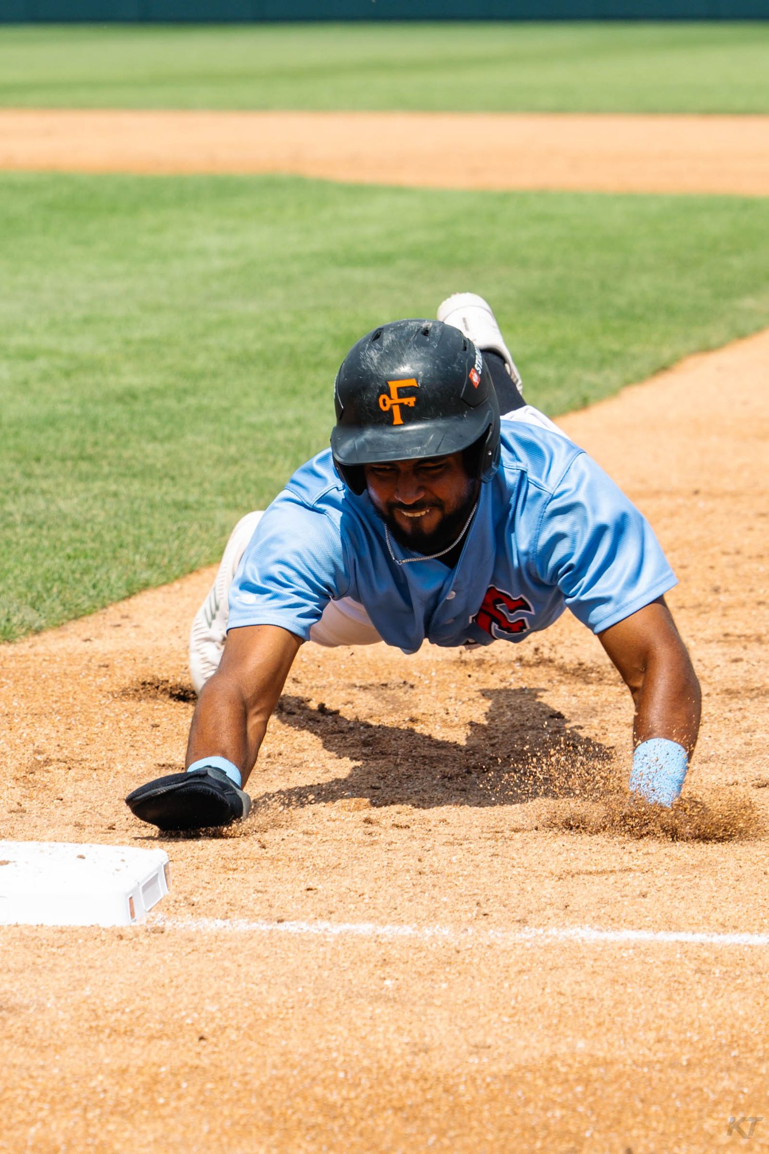 Baseball player in light blue jersey diving headfirst into base during a game.