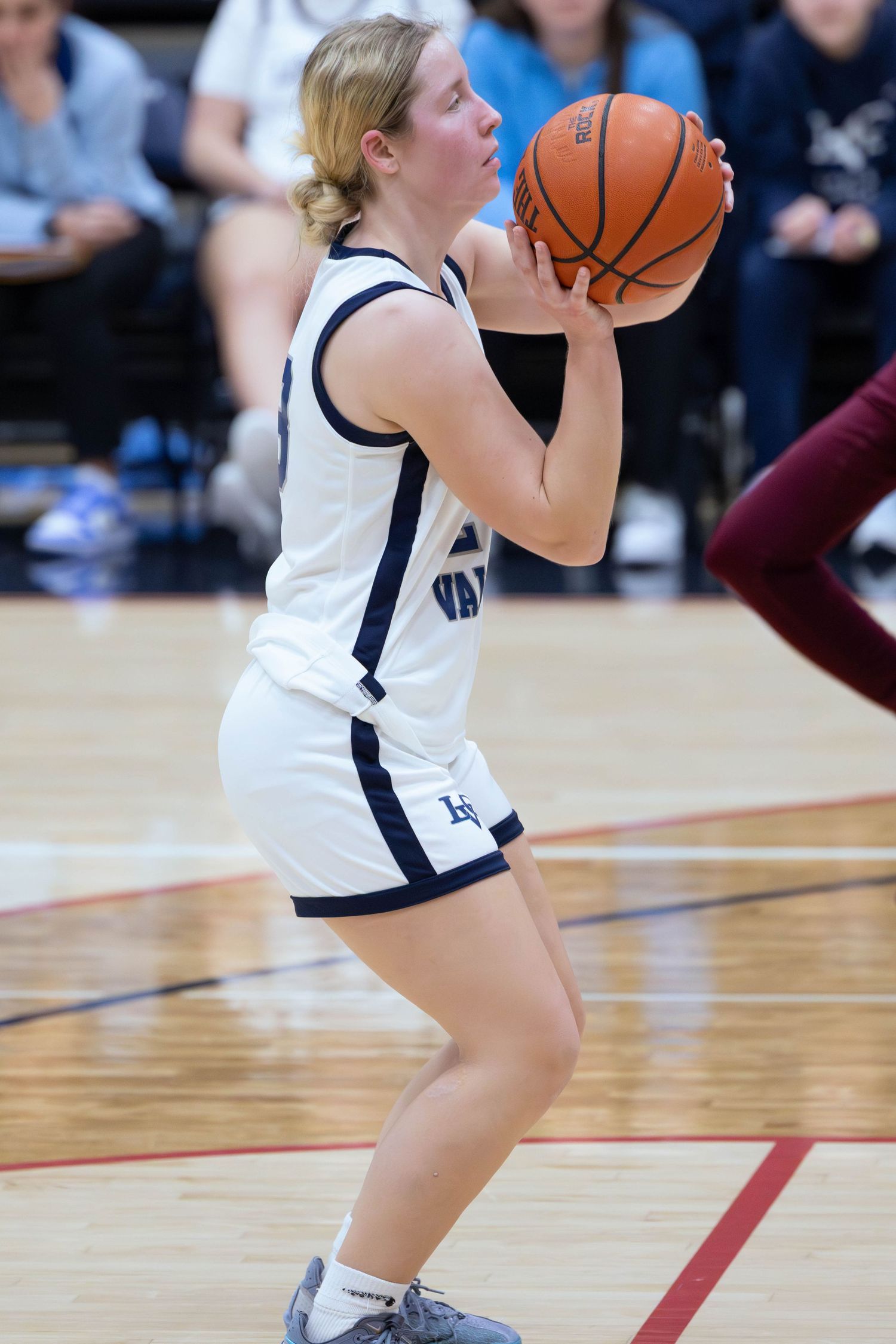 Female basketball player in white uniform prepares to shoot during an indoor game.