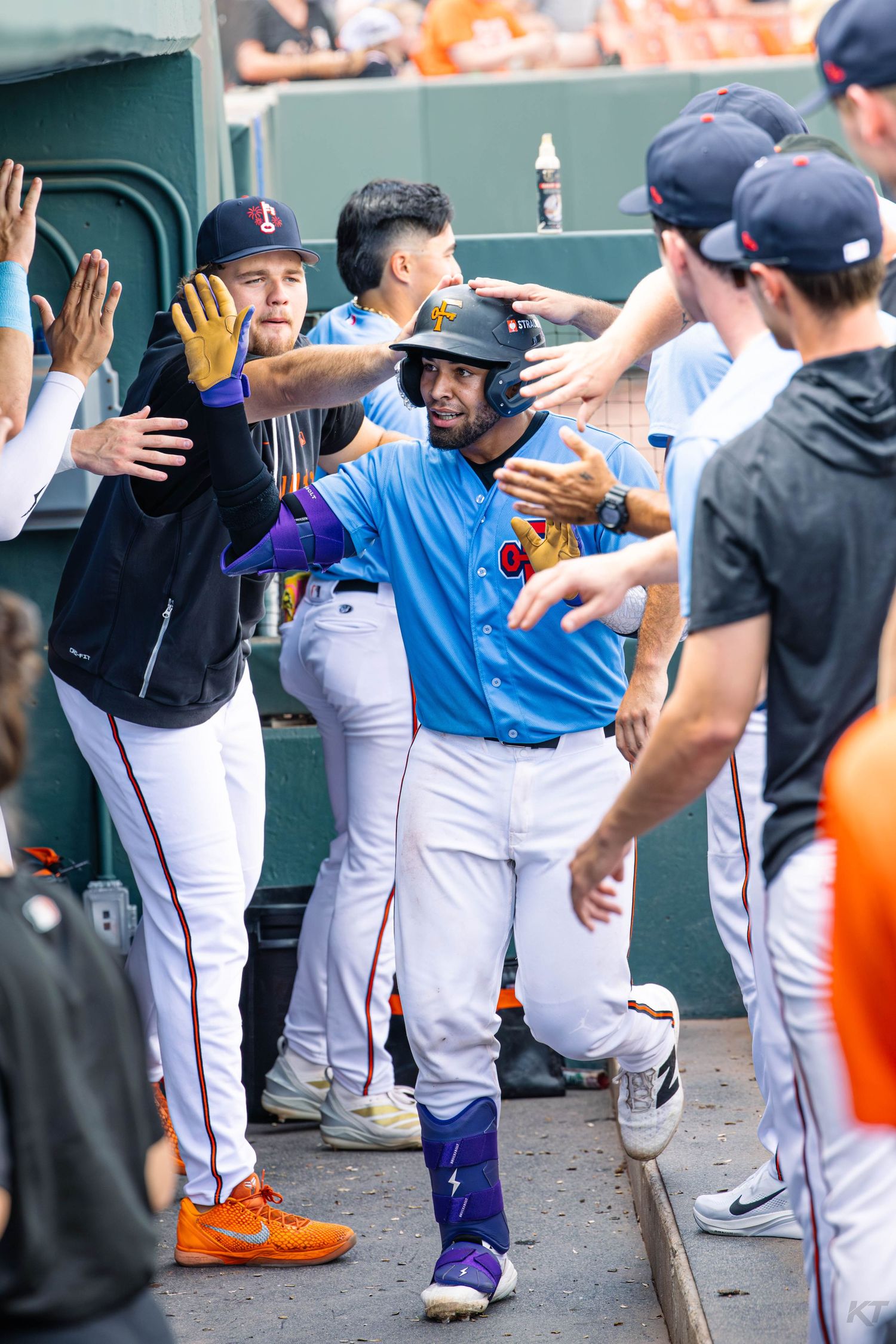 Baseball player celebrates in dugout with high-fives from teammates after scoring a run during a minor league game.