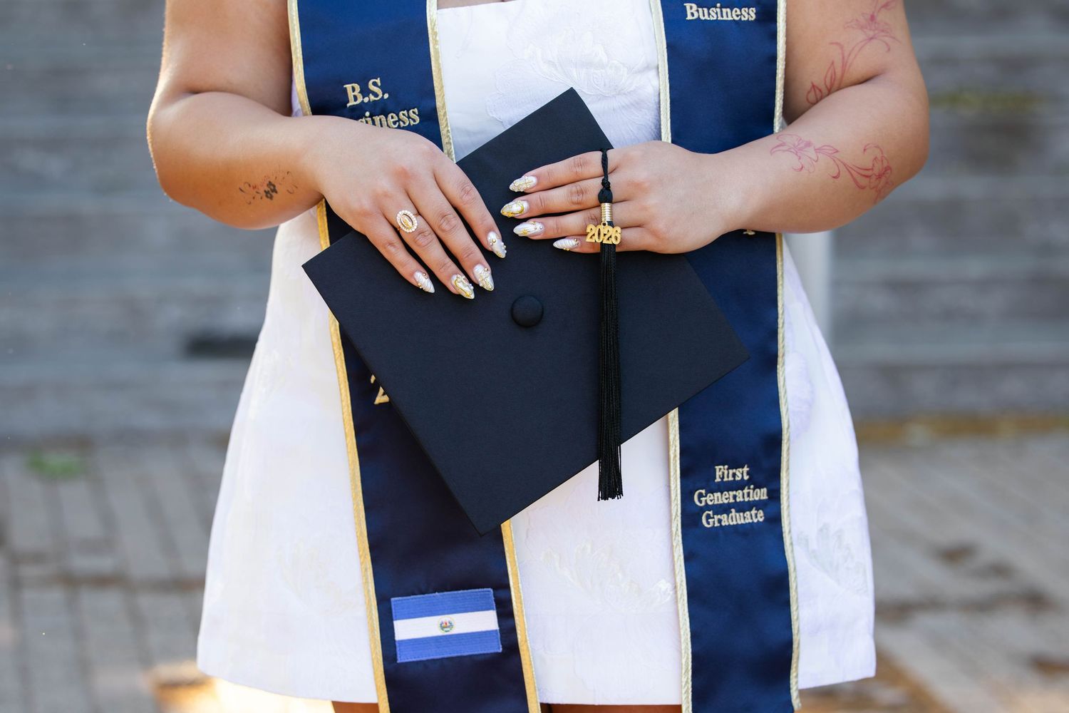 Close-up of graduate holding cap with B.S. Business and First Generation Graduate sash.