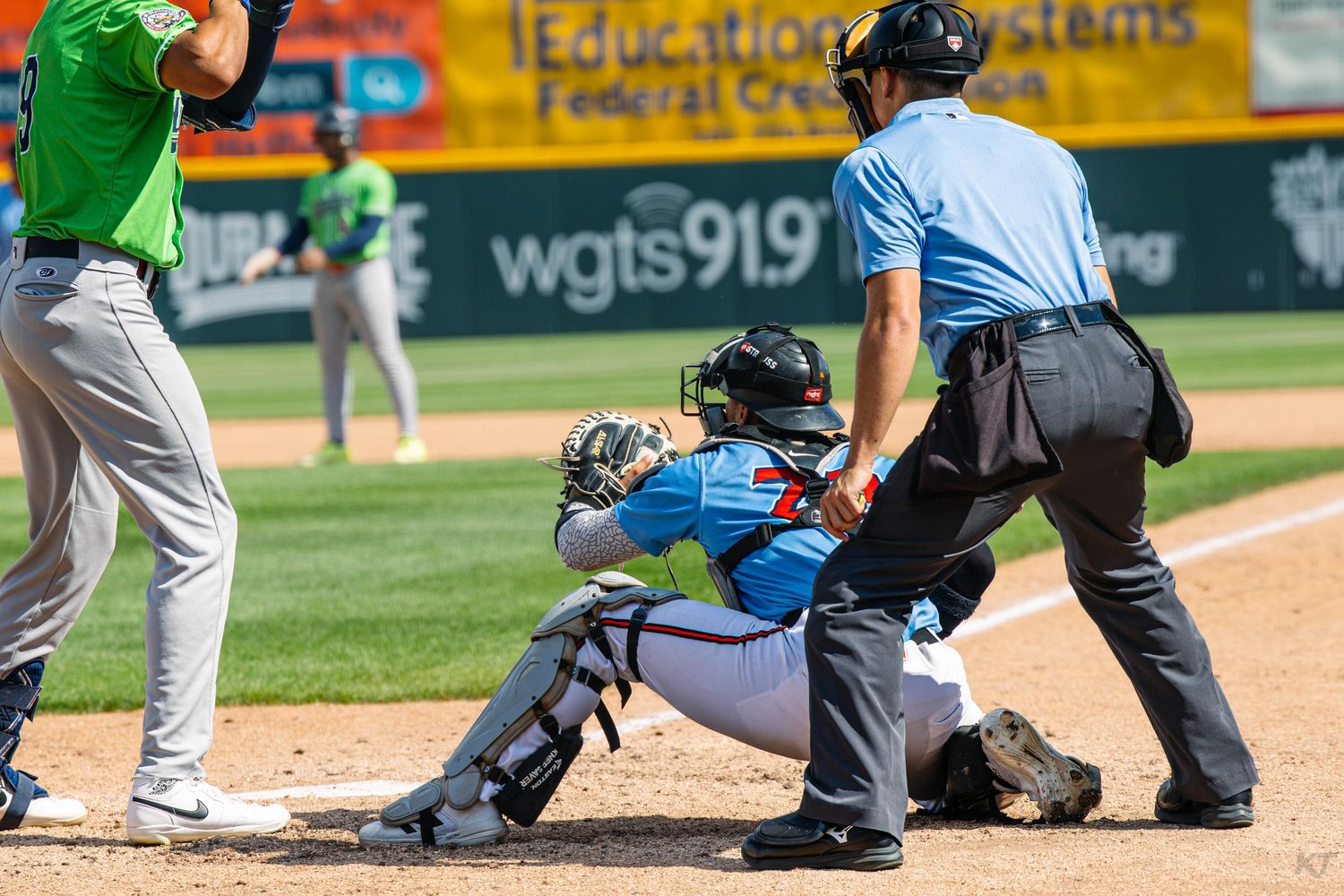 Baseball catcher tags out a runner at home plate as the umpire watches closely during a minor league game.