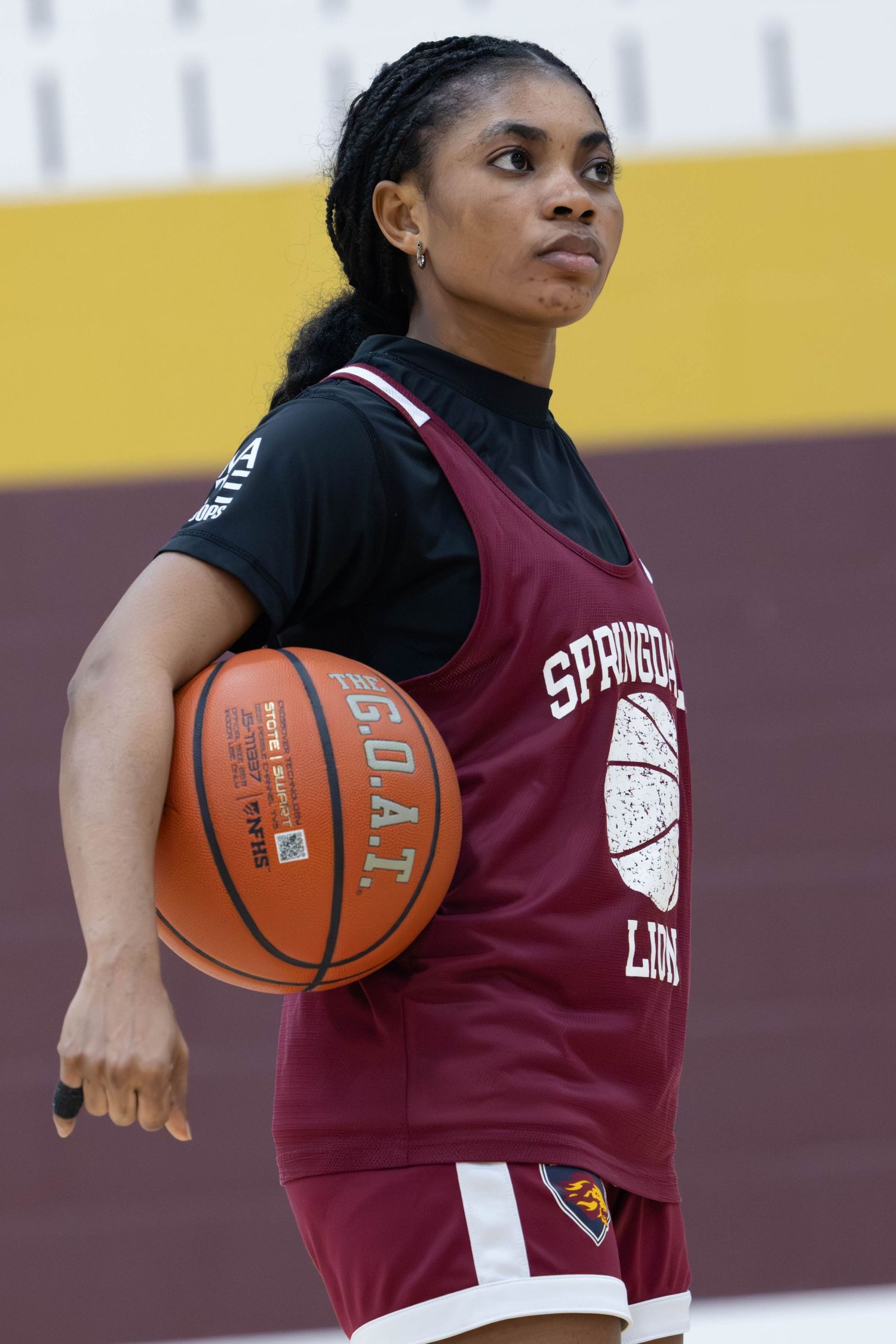 Female basketball player in Springdale Lions maroon jersey holds a basketball on an indoor court.