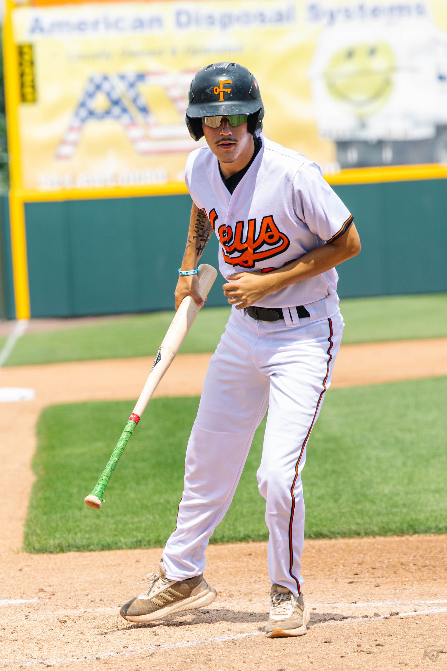 Baseball player in Keys uniform runs bases holding bat during sunny game near American Disposal Systems ad.