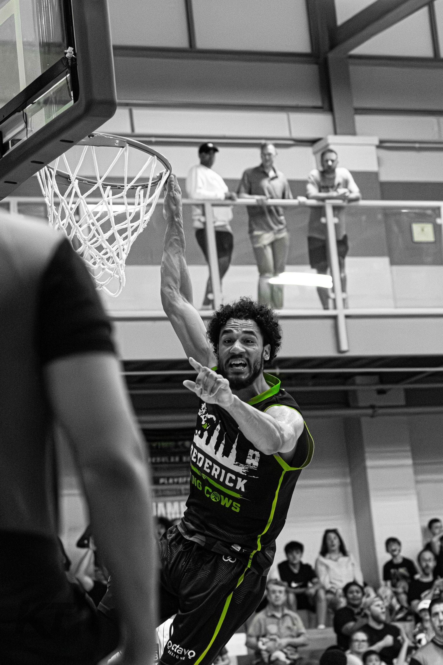 Frederick Crows basketball player dunking during a game, captured in dramatic black and white with green jersey accents.