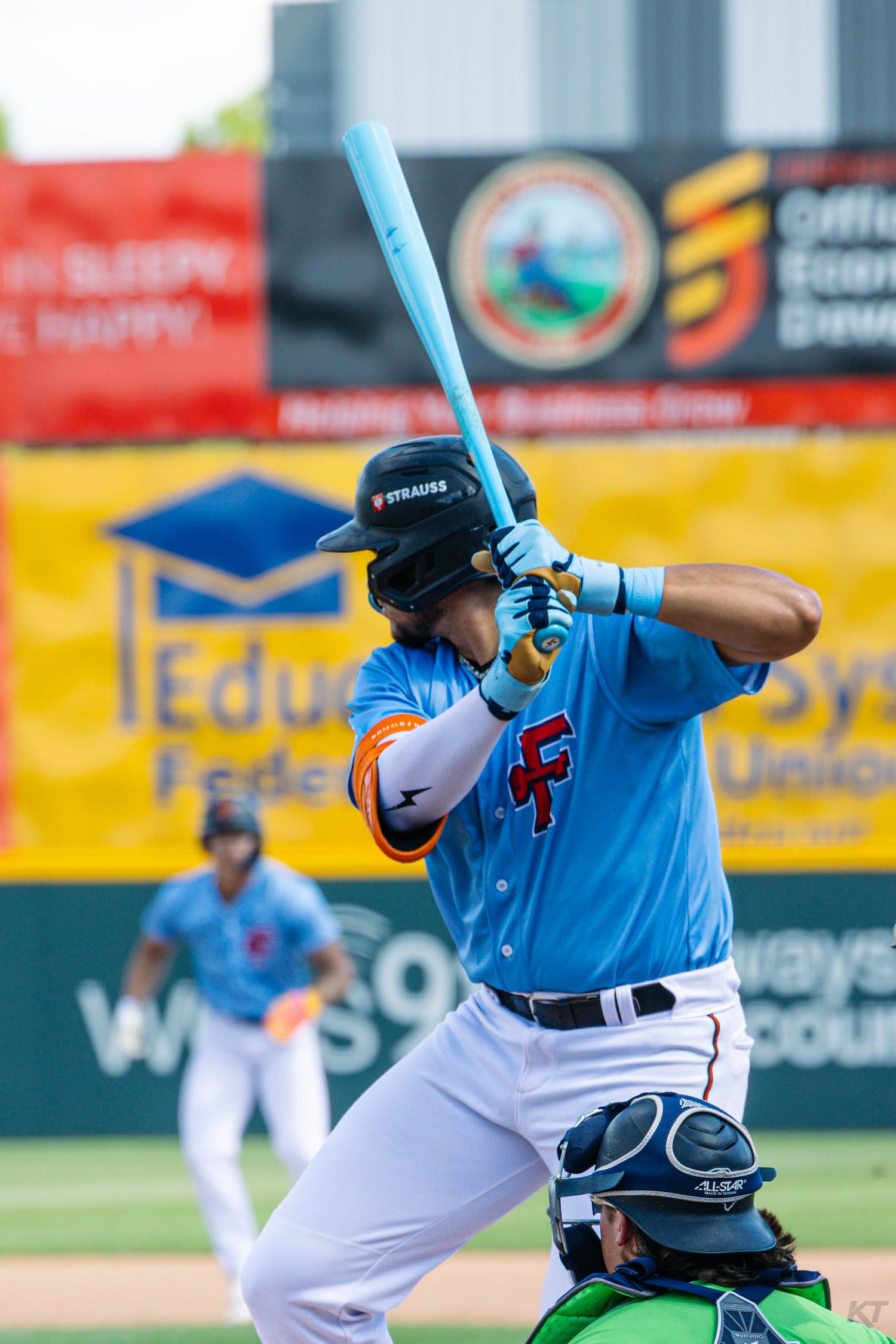 Minor league baseball batter in blue CF jersey assumes batting stance at home plate during a game.