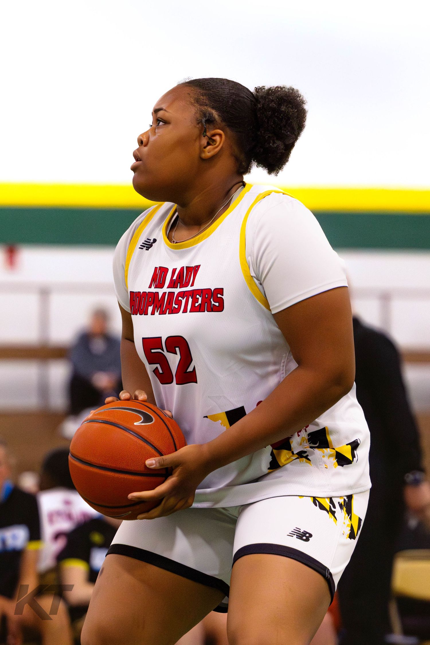 Female basketball player #52 in white MD Lady Jumpmasters uniform holds ball during indoor game.