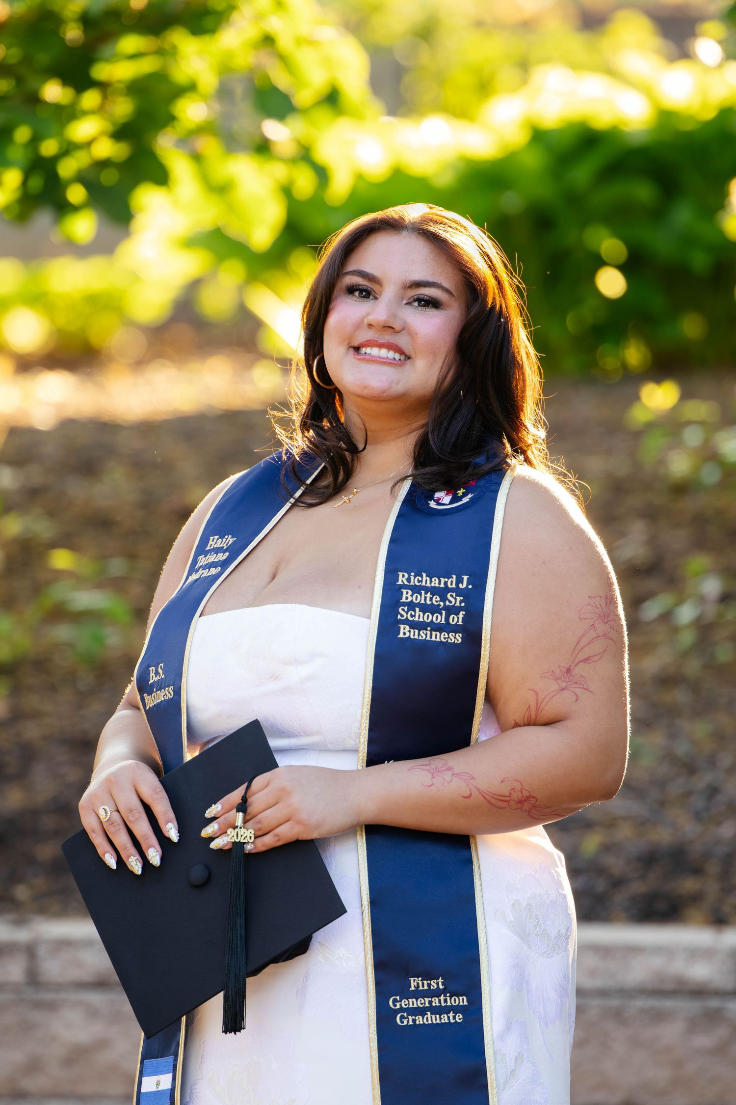 Smiling female graduate wearing Richard J. Bolte Sr. School of Business First Generation Graduate navy stole outdoors.