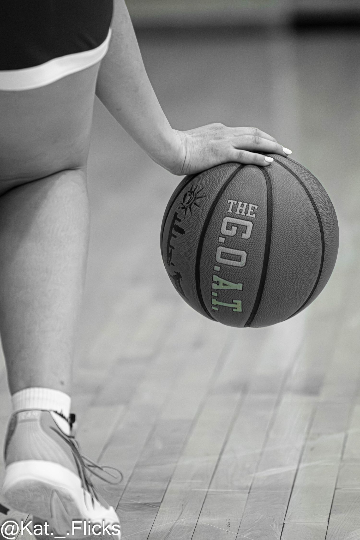 Black and white close-up of basketball player holding The G.O.A.T. branded basketball on hardwood court.