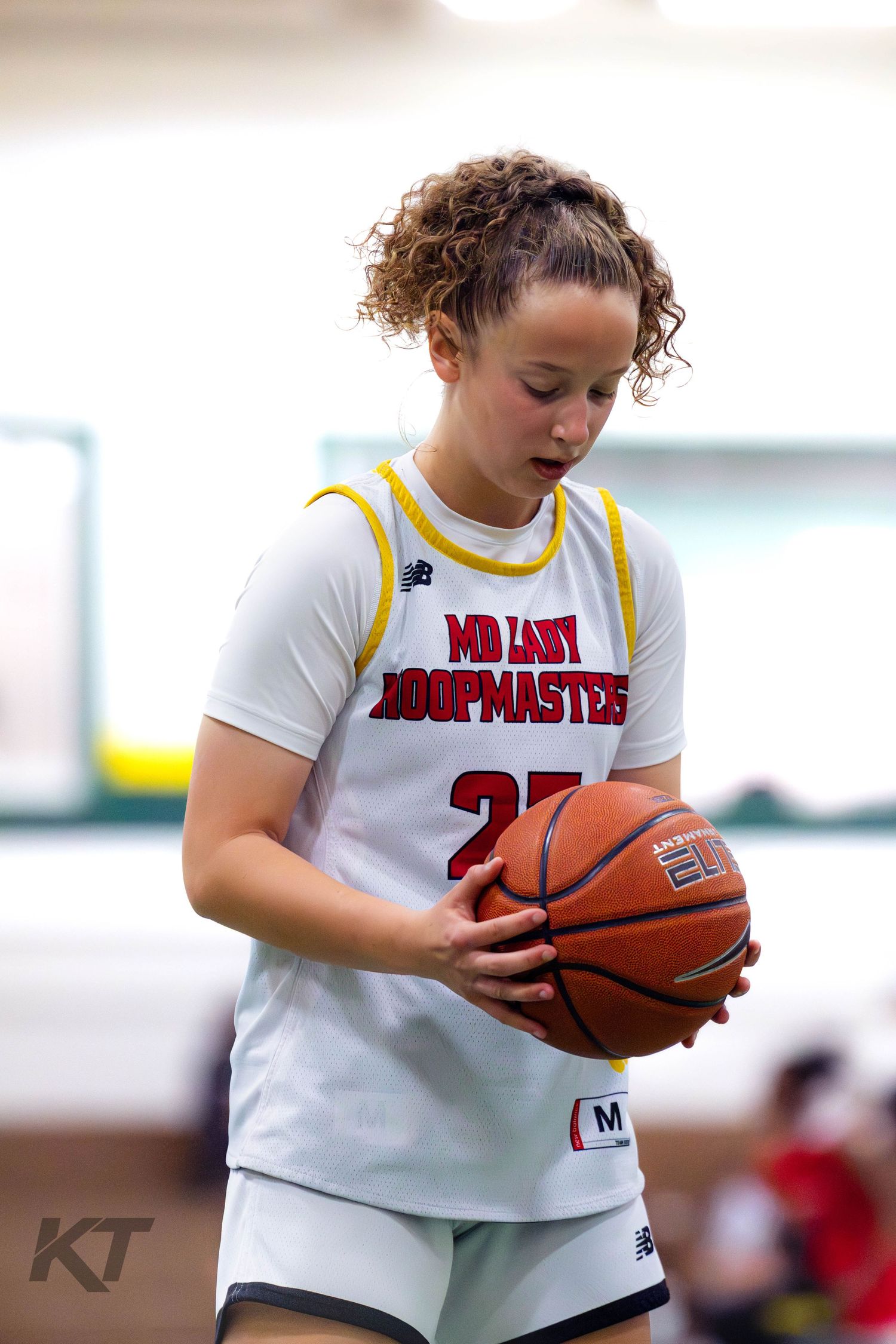 Young female basketball player in MD Lady Hoopmasters jersey holding a basketball during an indoor game.