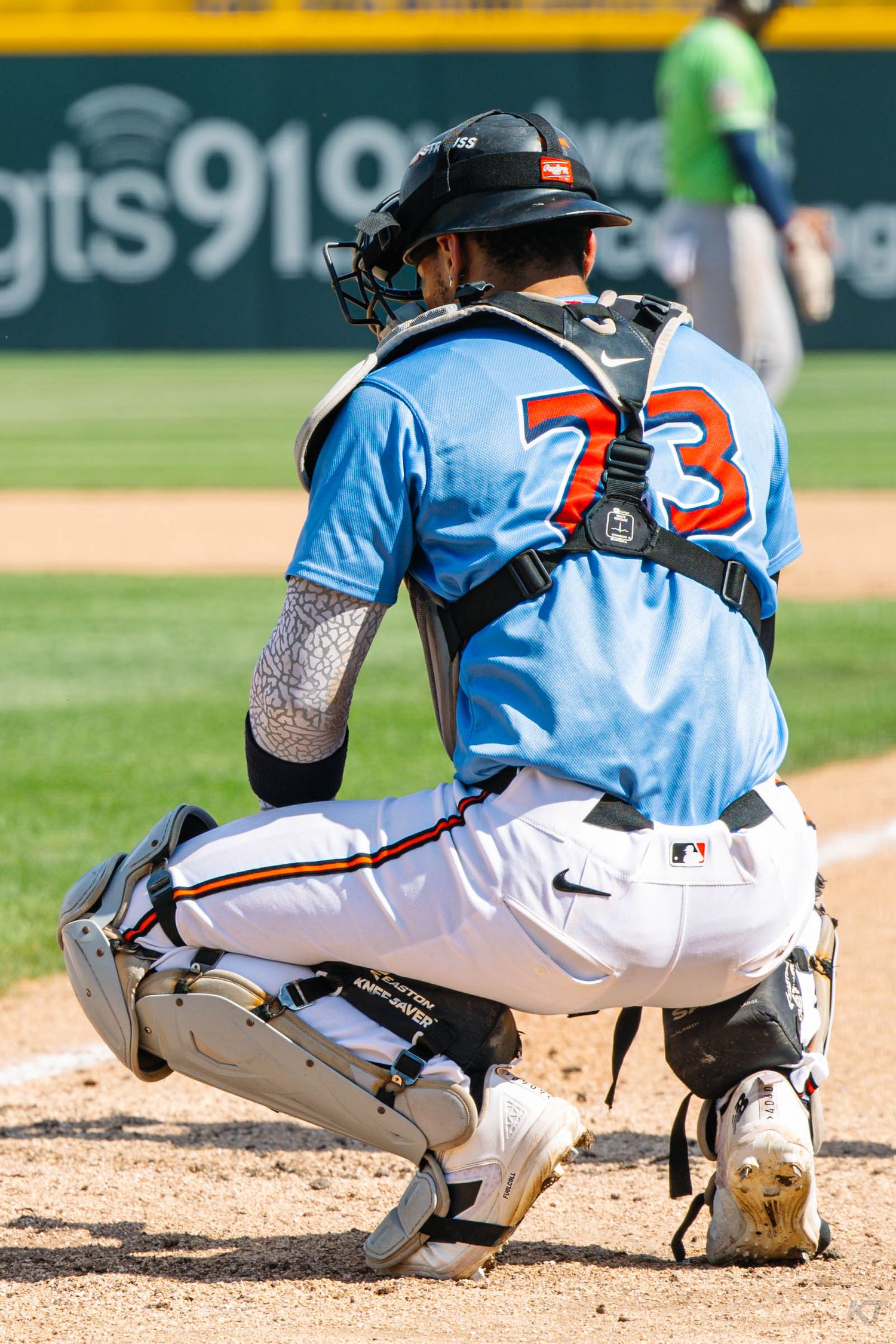 Baseball catcher in light blue jersey number 73 crouching at home plate wearing full protective gear.