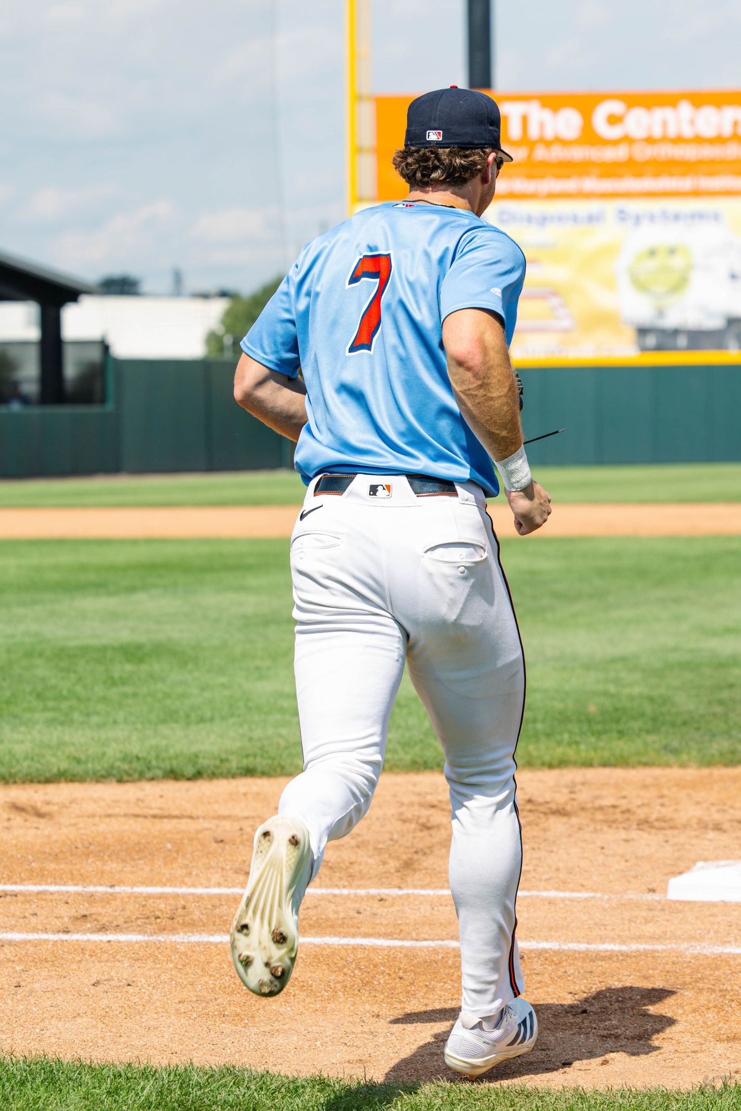 Baseball player number 7 in light blue uniform running bases on a sunny day at a professional baseball field.
