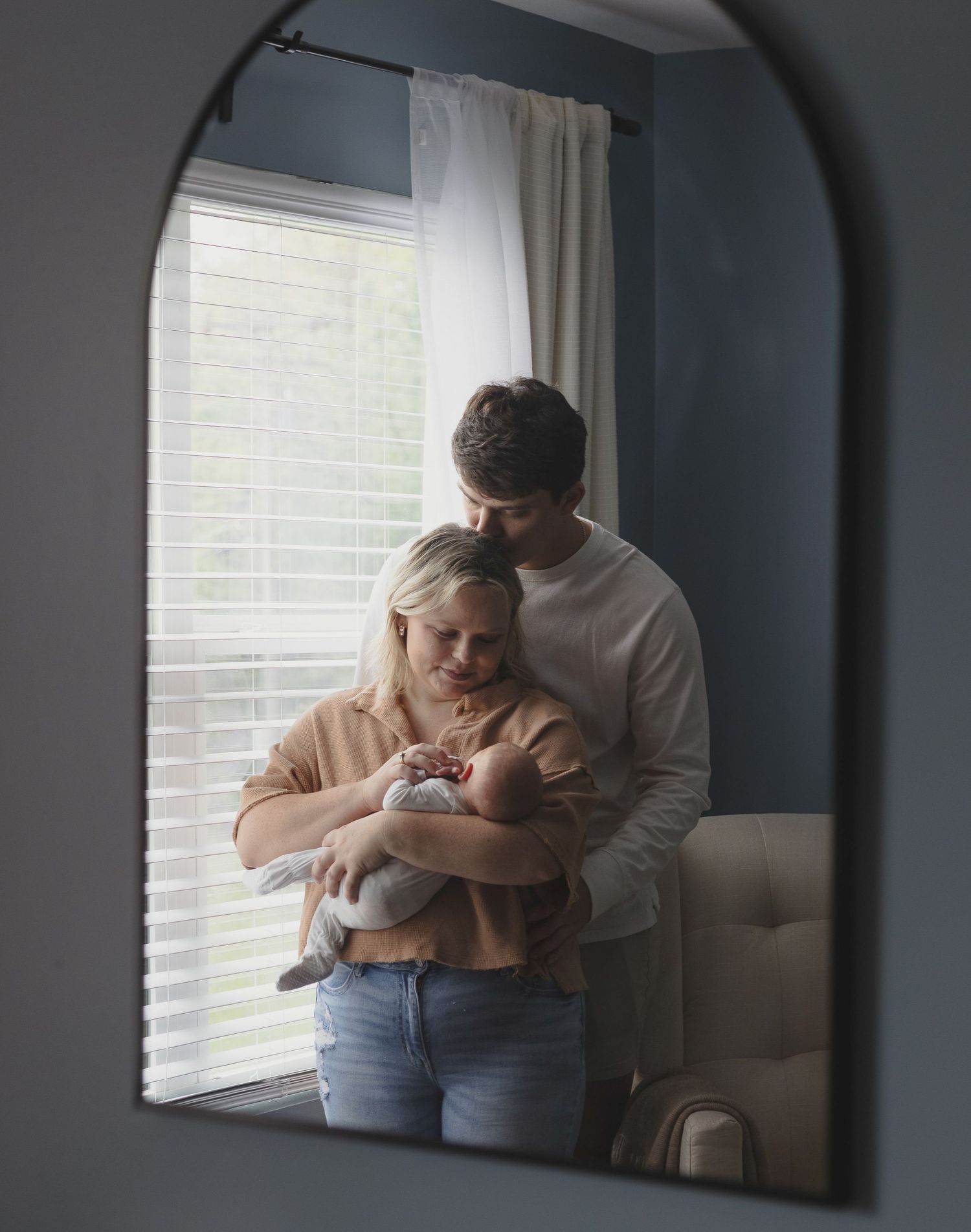 Mother holding her newborn by a window during a cozy in home newborn session. In knoxville, tn