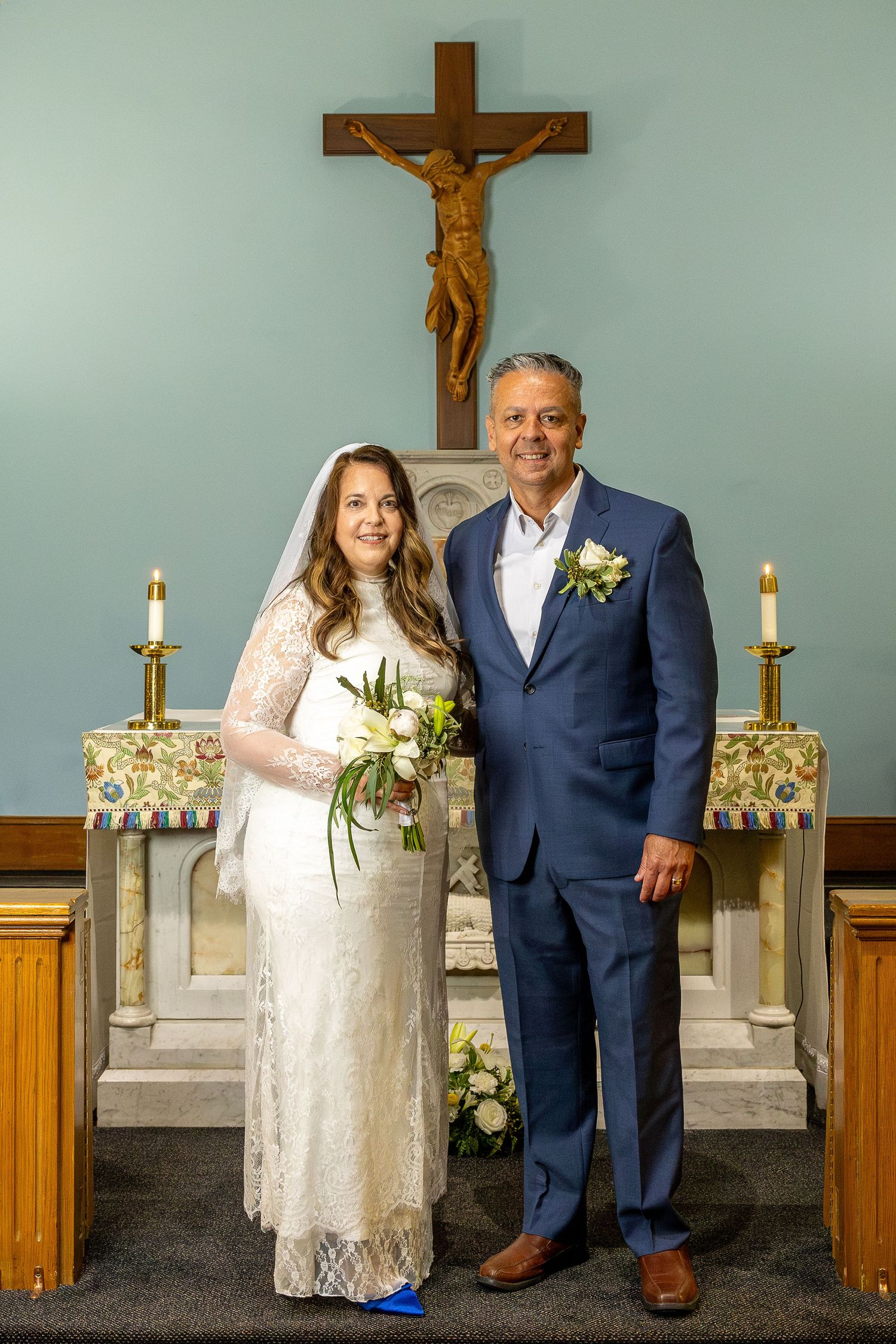 Catholic wedding portrait of a joyful bride and groom standing before the church altar and crucifix after their marriage ceremony.