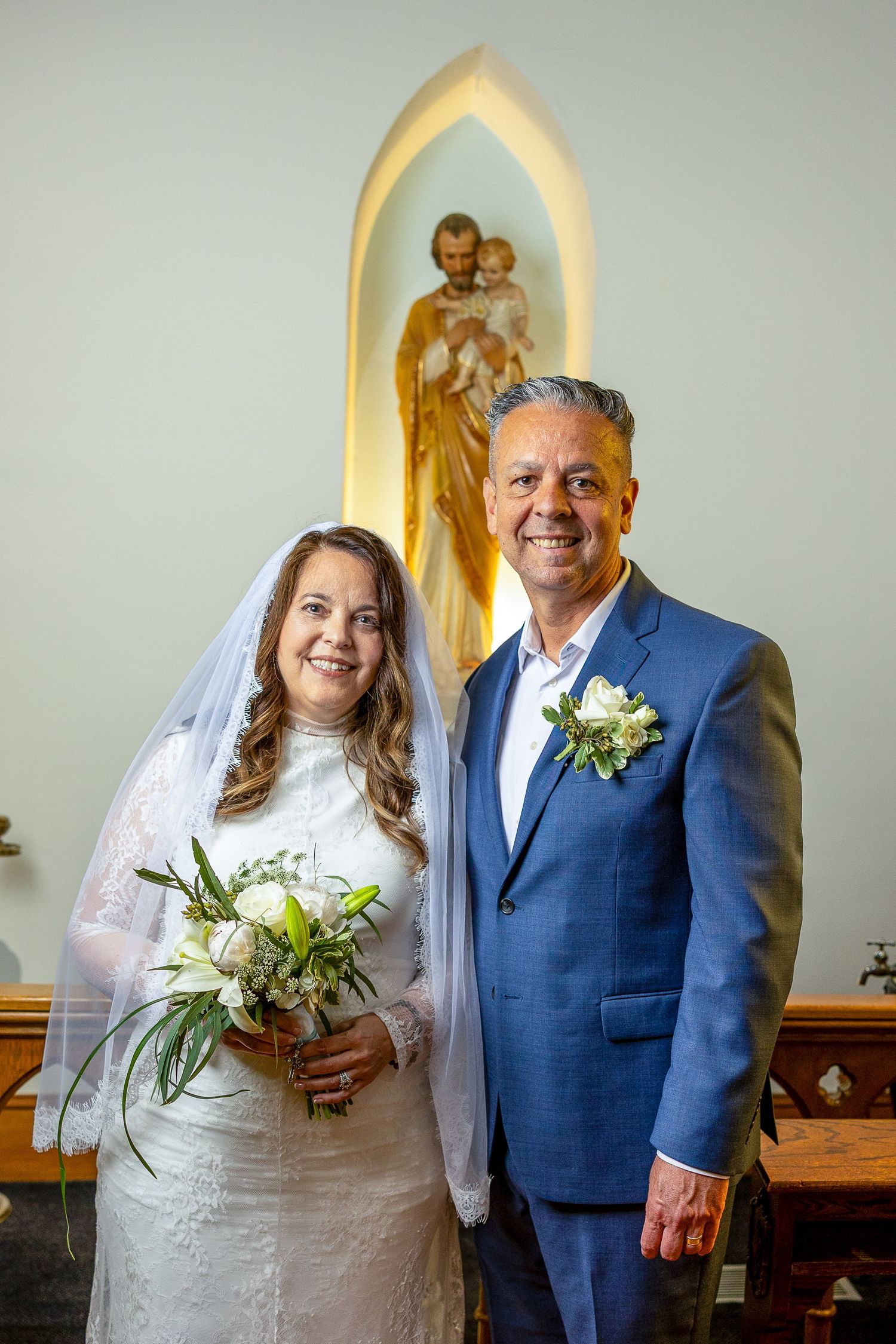 Catholic newlyweds share a joyful moment in front of St. Joseph after their wedding Mass, celebrating their sacred marriage.