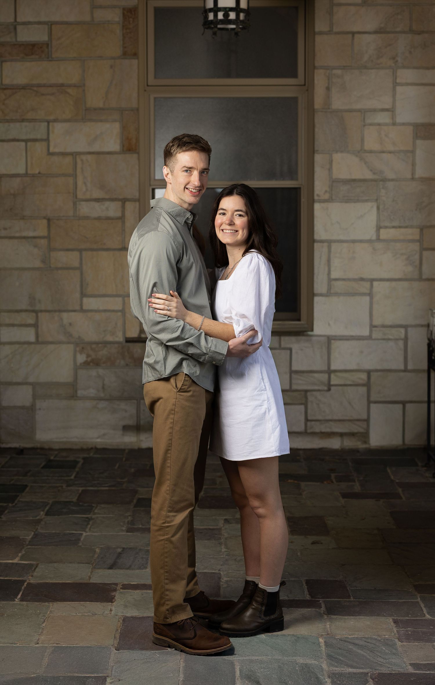 Engaged couple embraces inside a stone church corridor, smiling at the camera during a Catholic wedding engagement session.