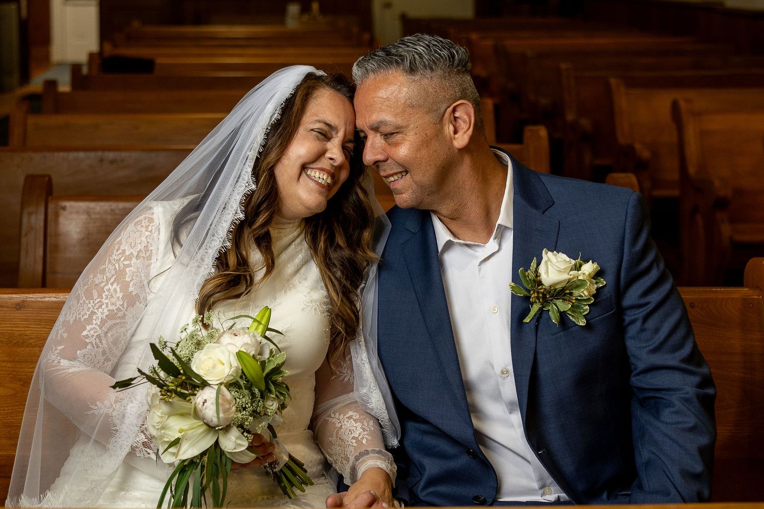 Catholic newlyweds share a joyful moment in a church pew after their wedding Mass, celebrating their sacred marriage.
