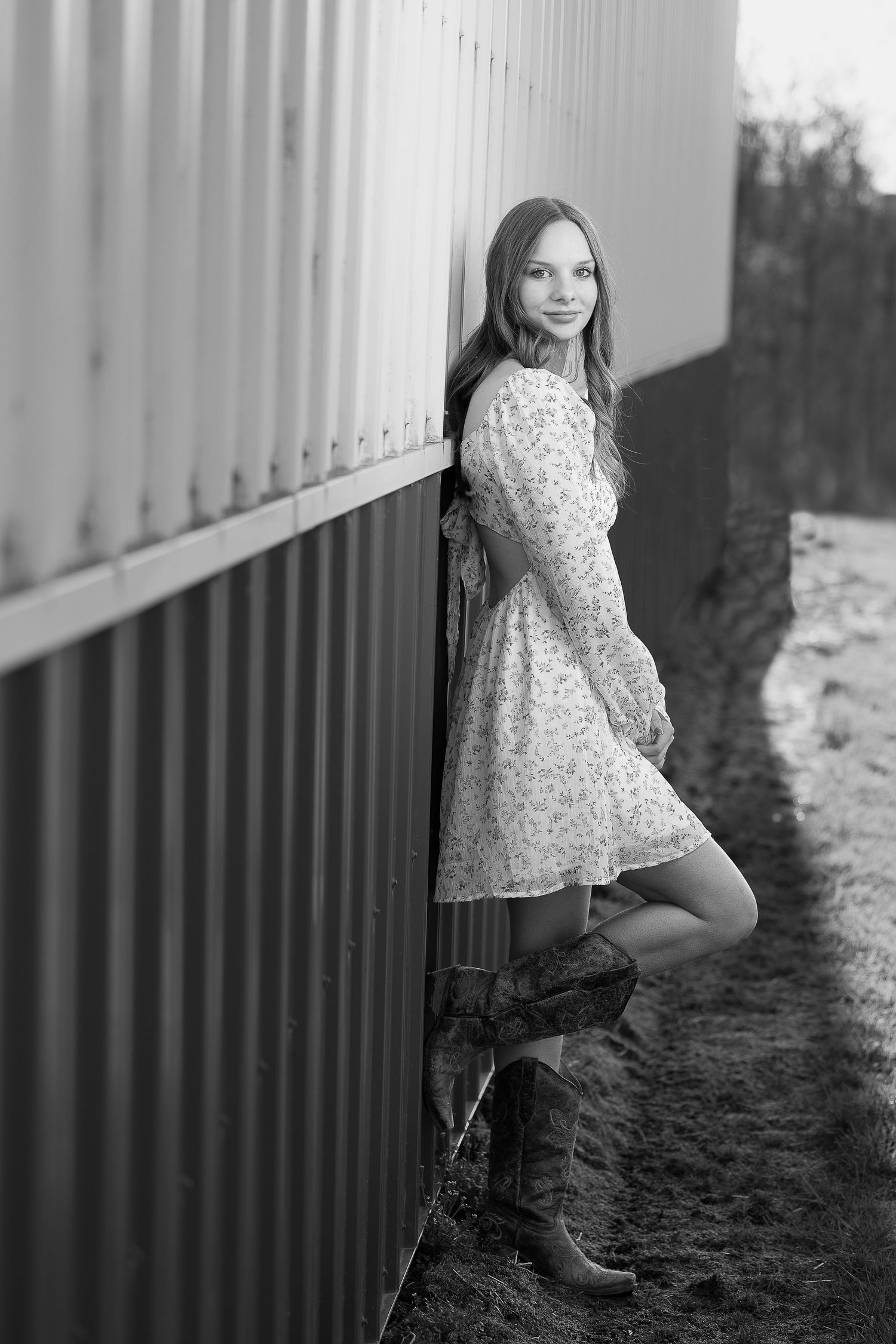 College graduate celebrates outdoors, leaning against a barn in Maryland.