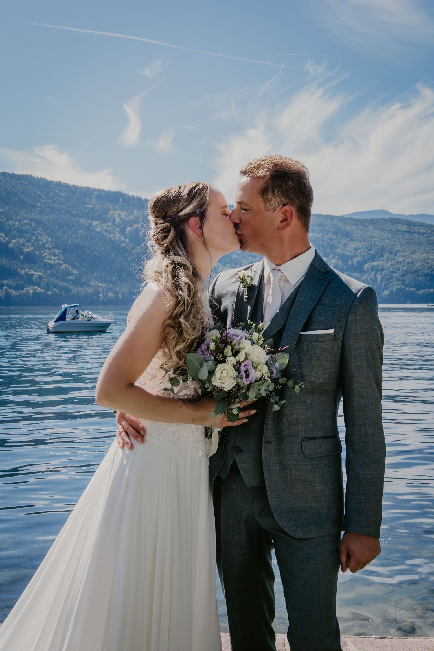 A romantic lakeside wedding photo shoot with mountains and blue water in the background.