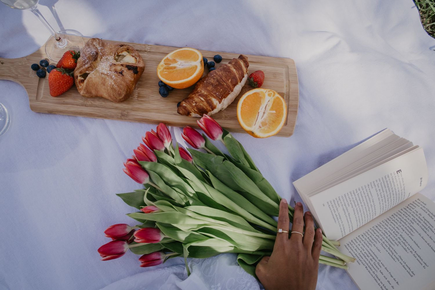 Fresh tulips and citrus slices arranged on a white surface with a book for a cozy spring reading setup.