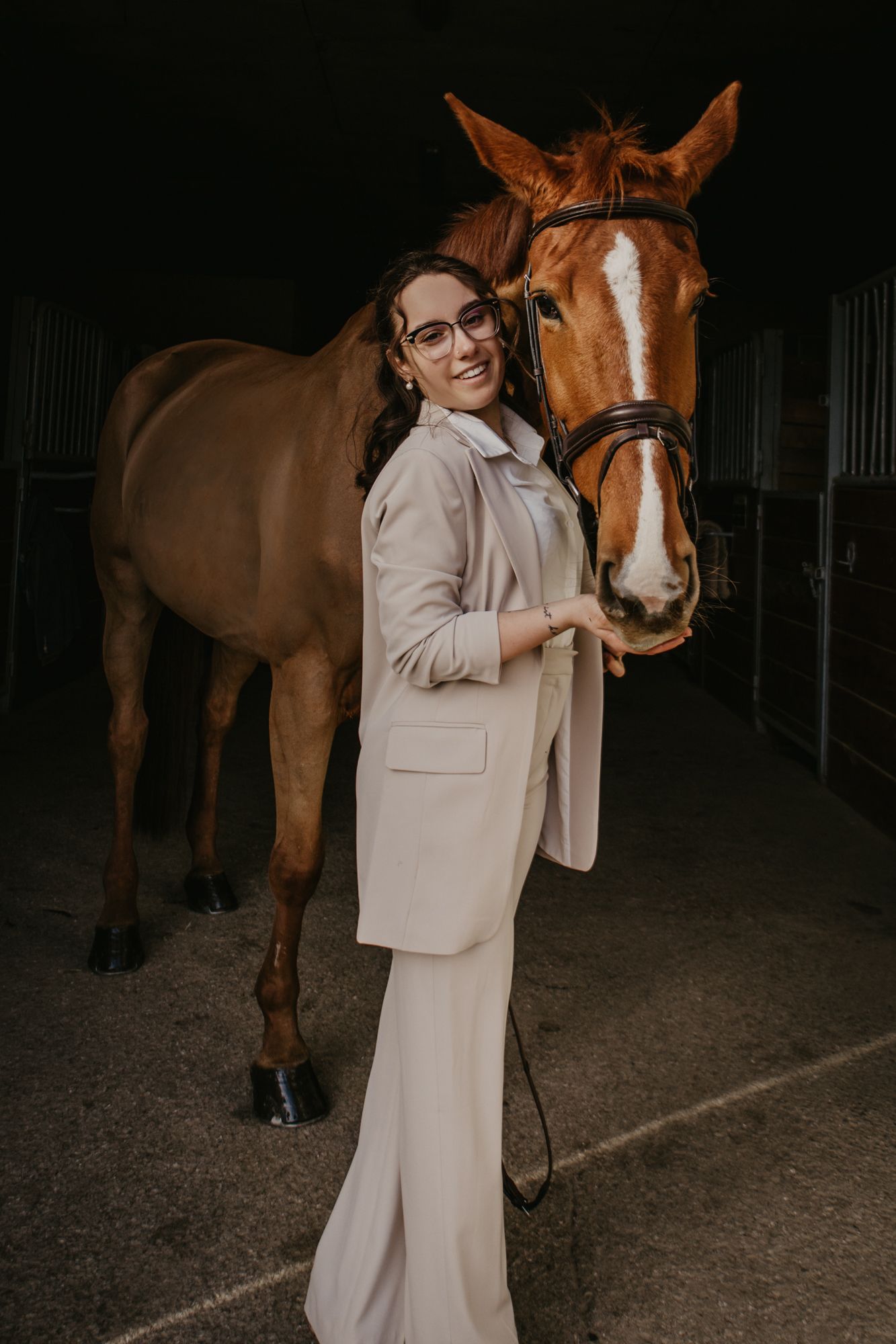 Moody indoor stable photos showing affectionate interaction between a horse and person in light clothing.