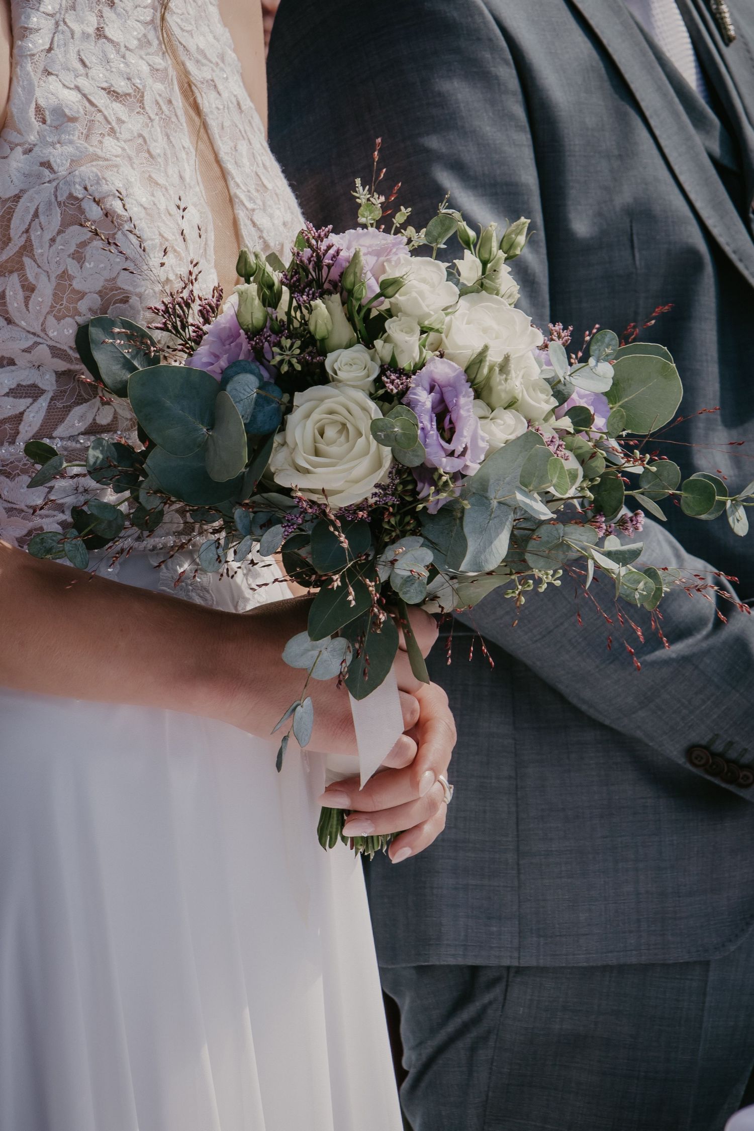 Wedding bouquet detail featuring white roses, purple flowers, and eucalyptus leaves.