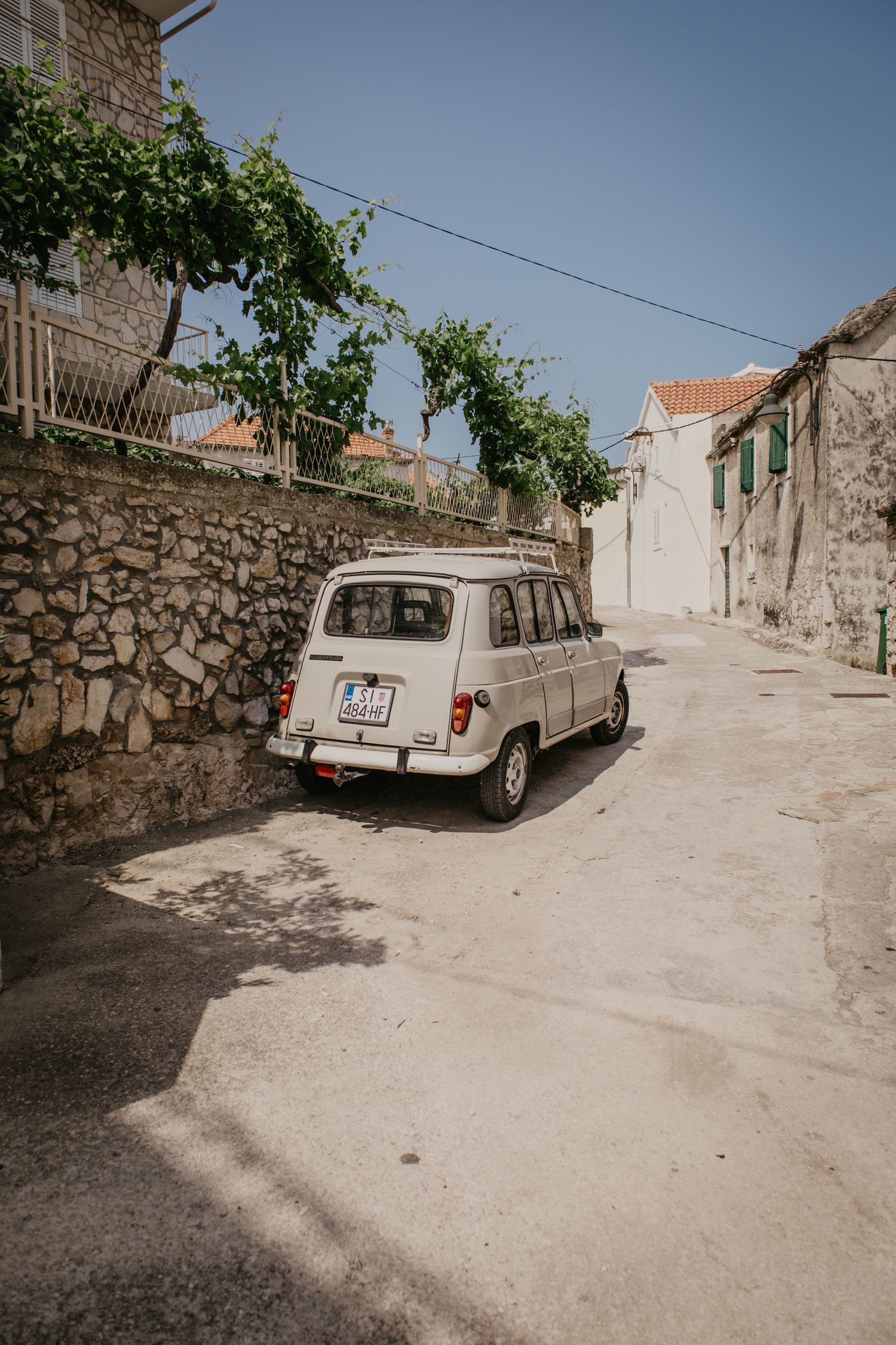 Narrow stone-paved street with parked cars in a Mediterranean village.