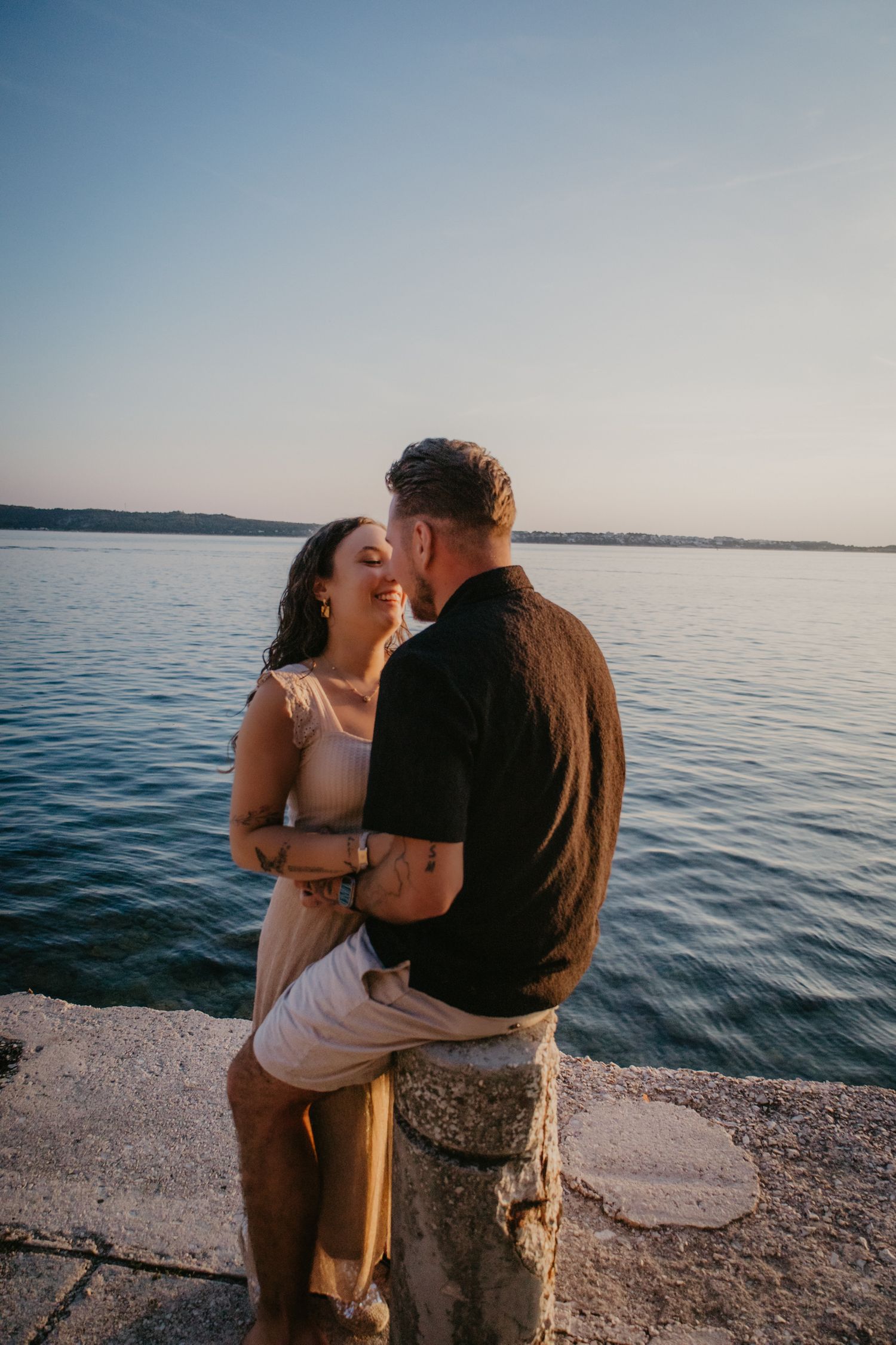 Two people share a joyful moment together on a lakefront pier during sunset.