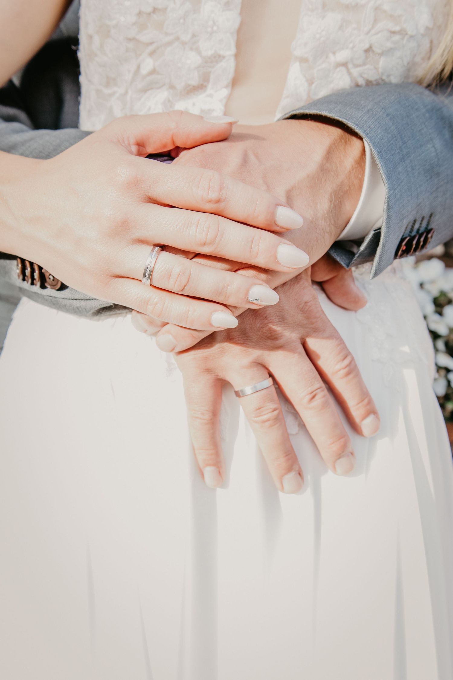 Close-up of hands with wedding rings resting on white fabric.