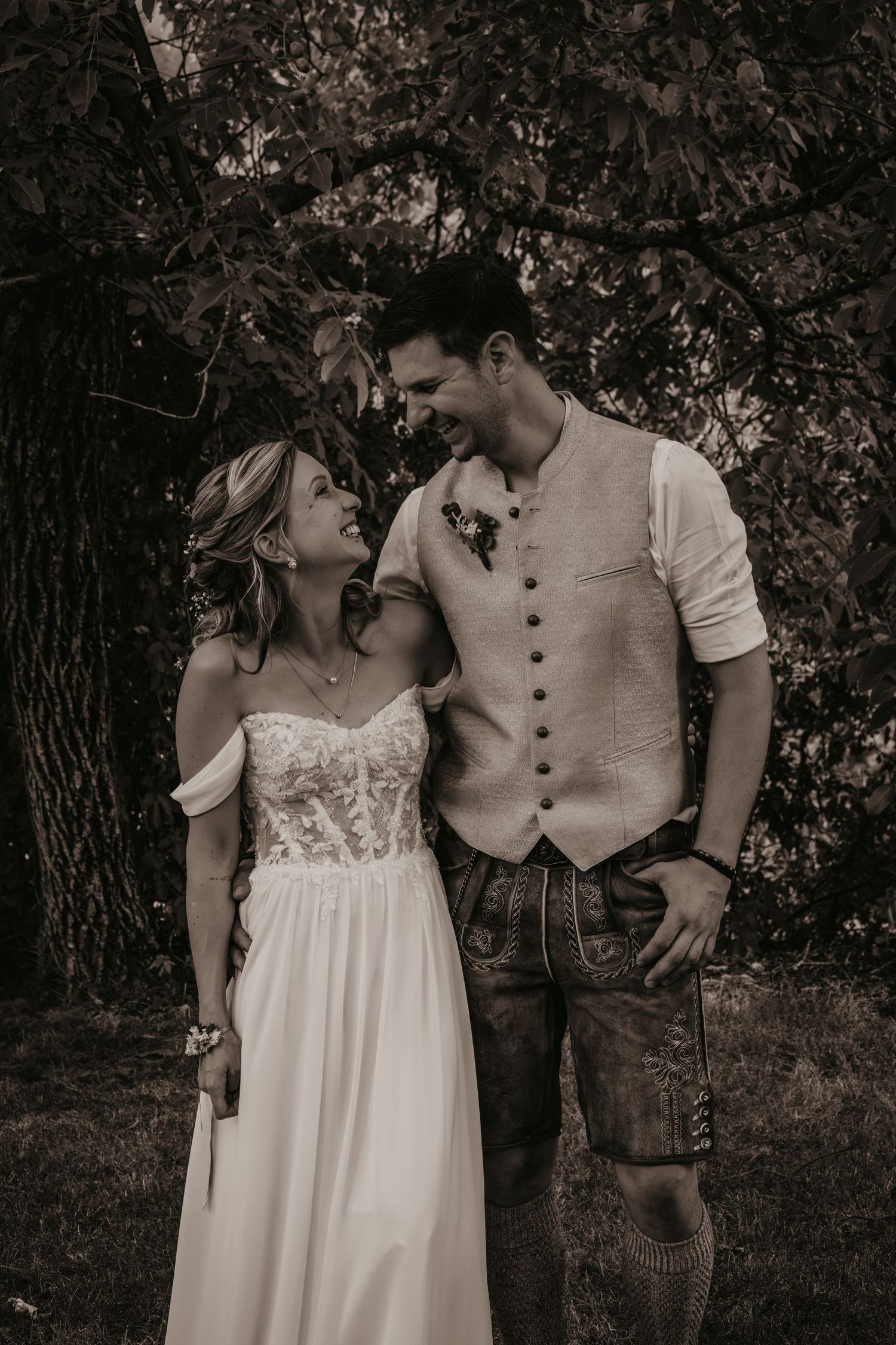 Black and white photo of smiling bride and groom in traditional Bavarian attire outdoors.