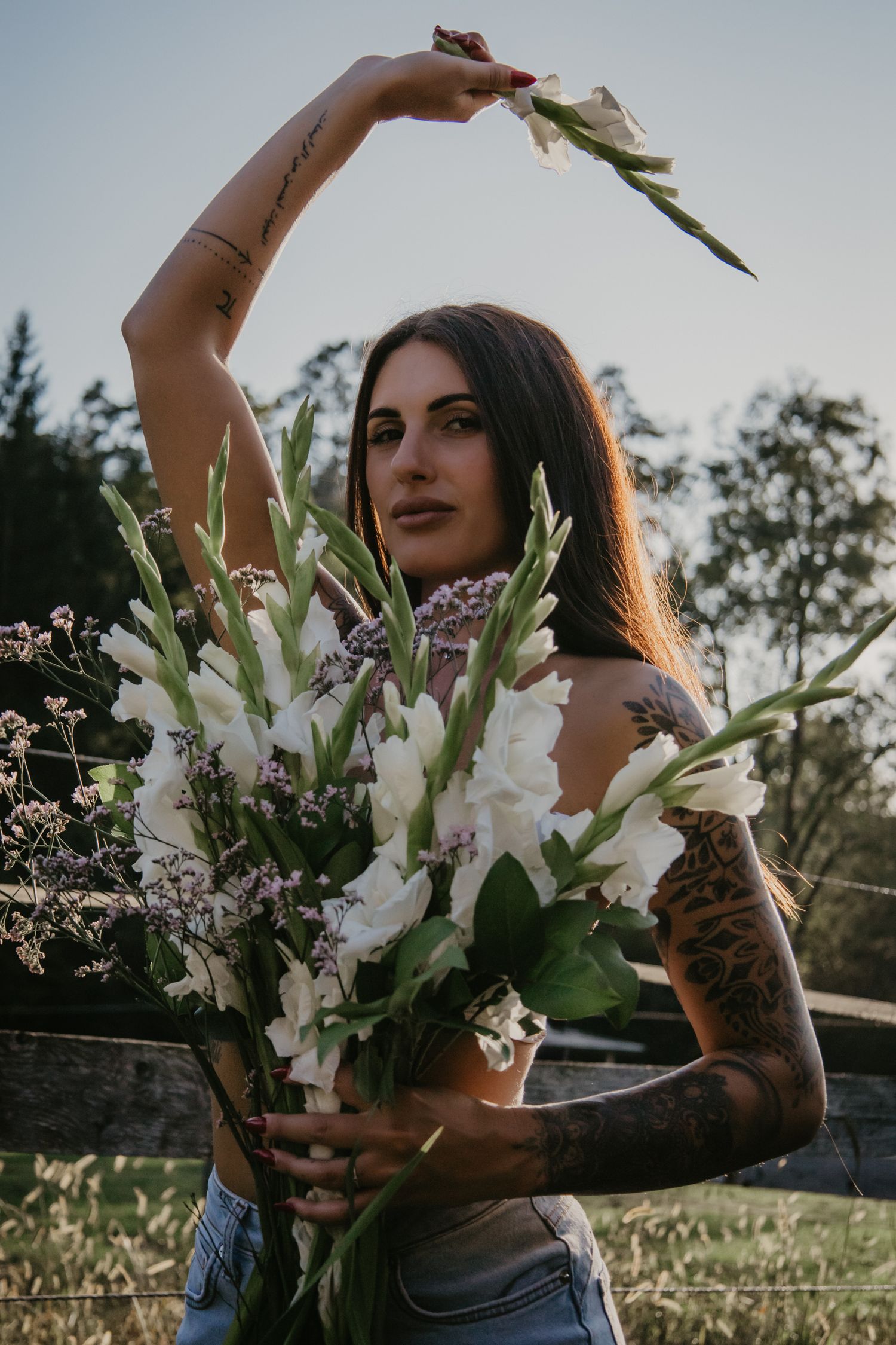 Candid moment with white gladiolus bouquet and tattoos in natural outdoor setting.