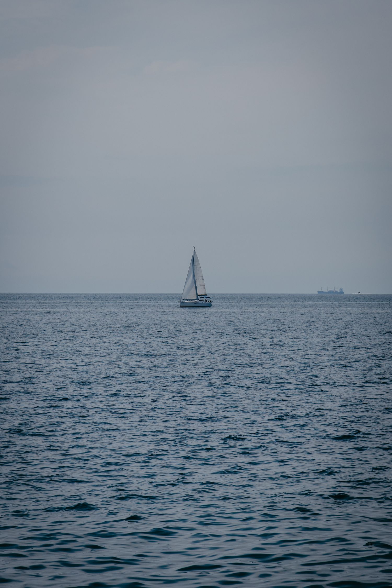 Distant fishing boat on calm blue waters under an overcast sky.
