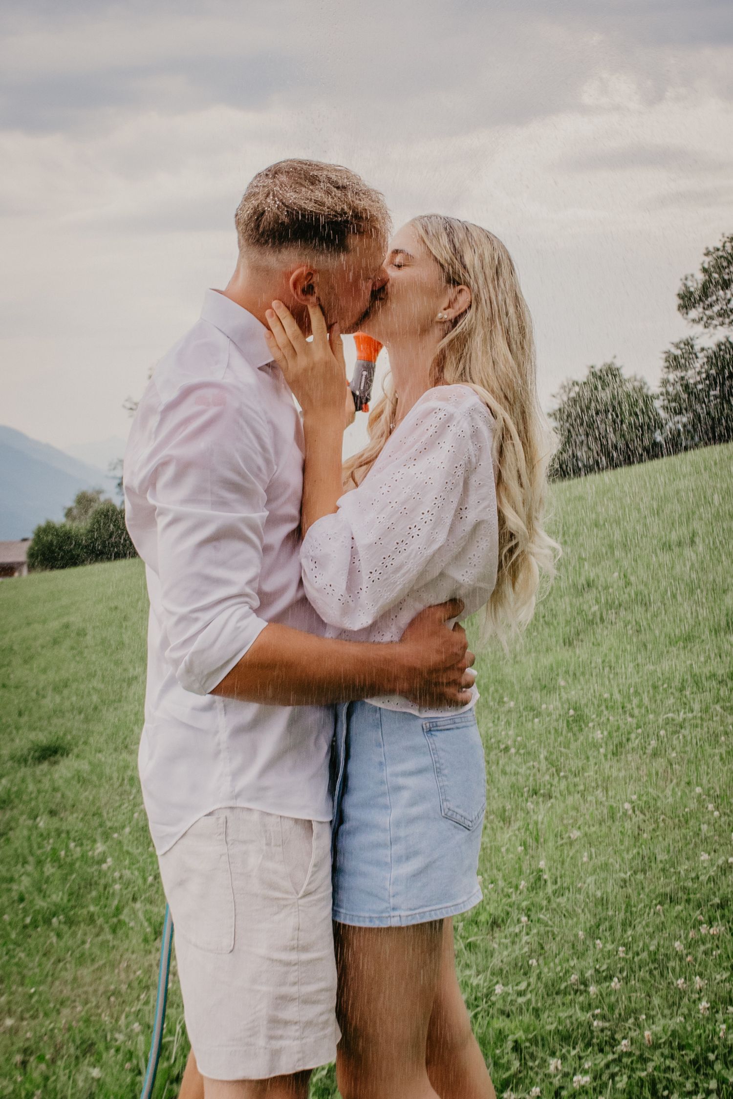 A couple sharing a romantic kiss in a green meadow, the woman in a white blouse and denim skirt, the man in light casual wear.