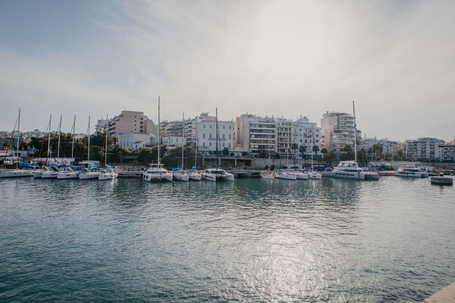 Panoramic view of sailboats moored in an Athens marina with calm waters.
