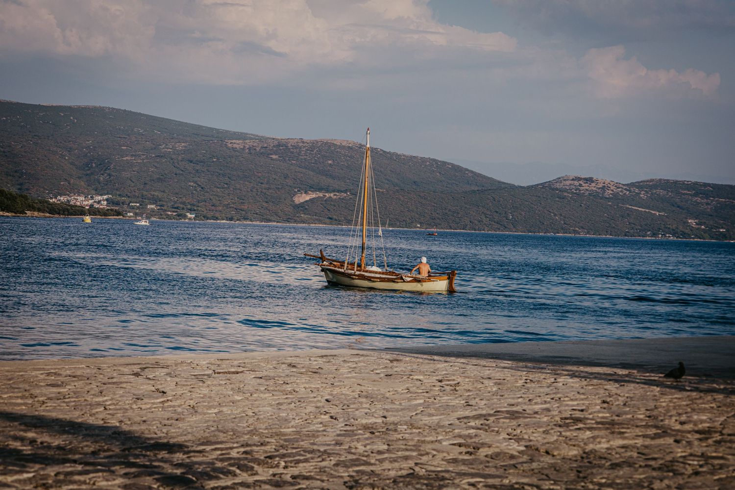 Scenic coastal view with sailboats anchored in calm blue waters near mountainous shoreline.